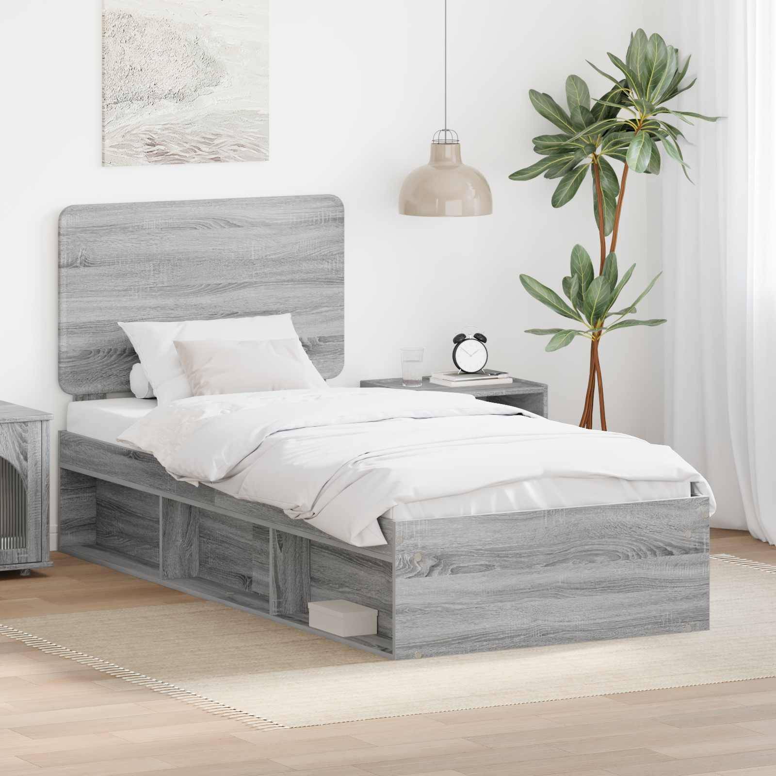 Ein Schlafzimmerszenario mit einem grauem Holzbett, weißer Bettwäsche, einem kleinen Nachttisch, einer Topfpflanze, einer hängenden Lampe und einem Wandgemälde.