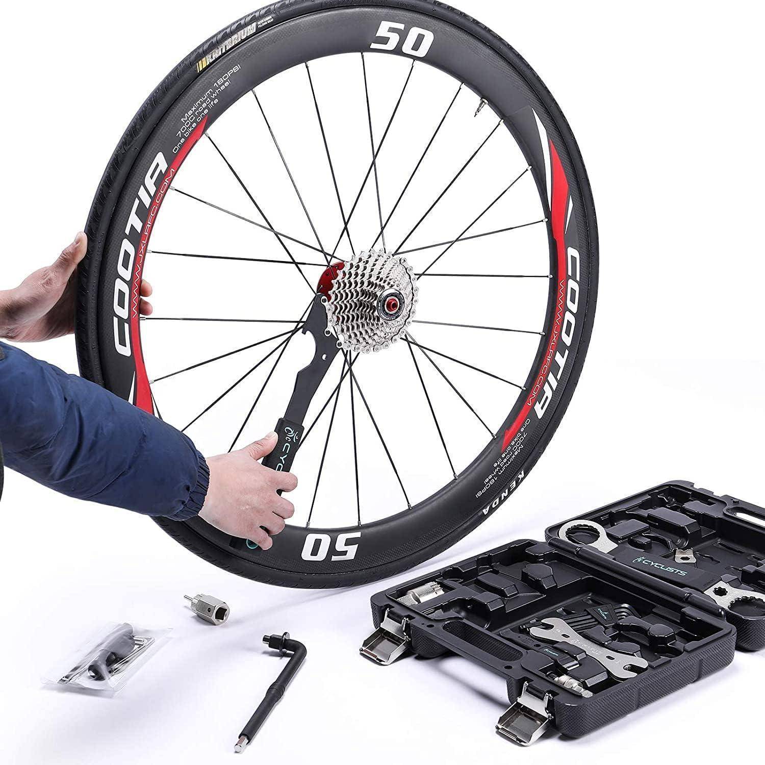 Eine Person hält ein Fahrradrad neben einer geöffneten Werkzeugkiste, die verschiedene Reparaturwerkzeuge auf einer weißen Oberfläche zeigt und damit Fahrradinstandhaltung andeutet.