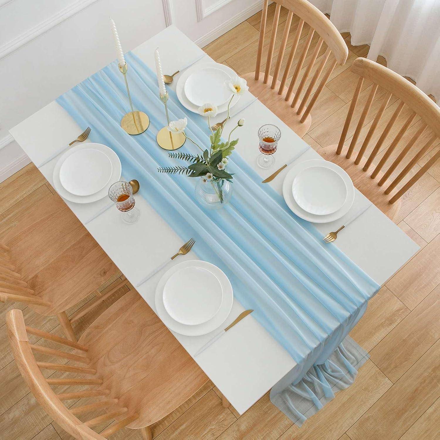 Esstisch für sechs Personen gedeckt mit weißen Tellern, goldenem Besteck und Gläsern. Ein blauer Tischläufer und ein kleines Blumengesteck dekorieren den Tisch.