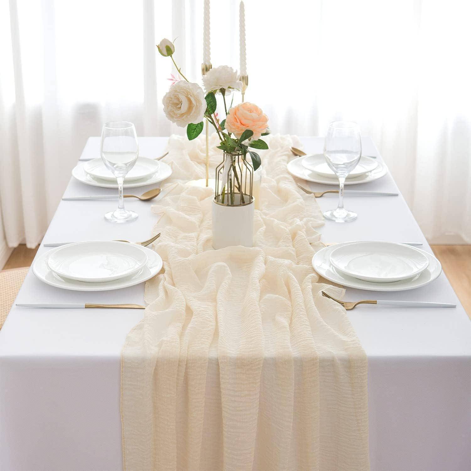 Elegante Tischdecke mit weißen Tellern, goldenen Bestecken und Weingläsern auf einem weißen Tischtuch. Ein Blumenarrangement mit Rosen befindet sich in der Mitte.