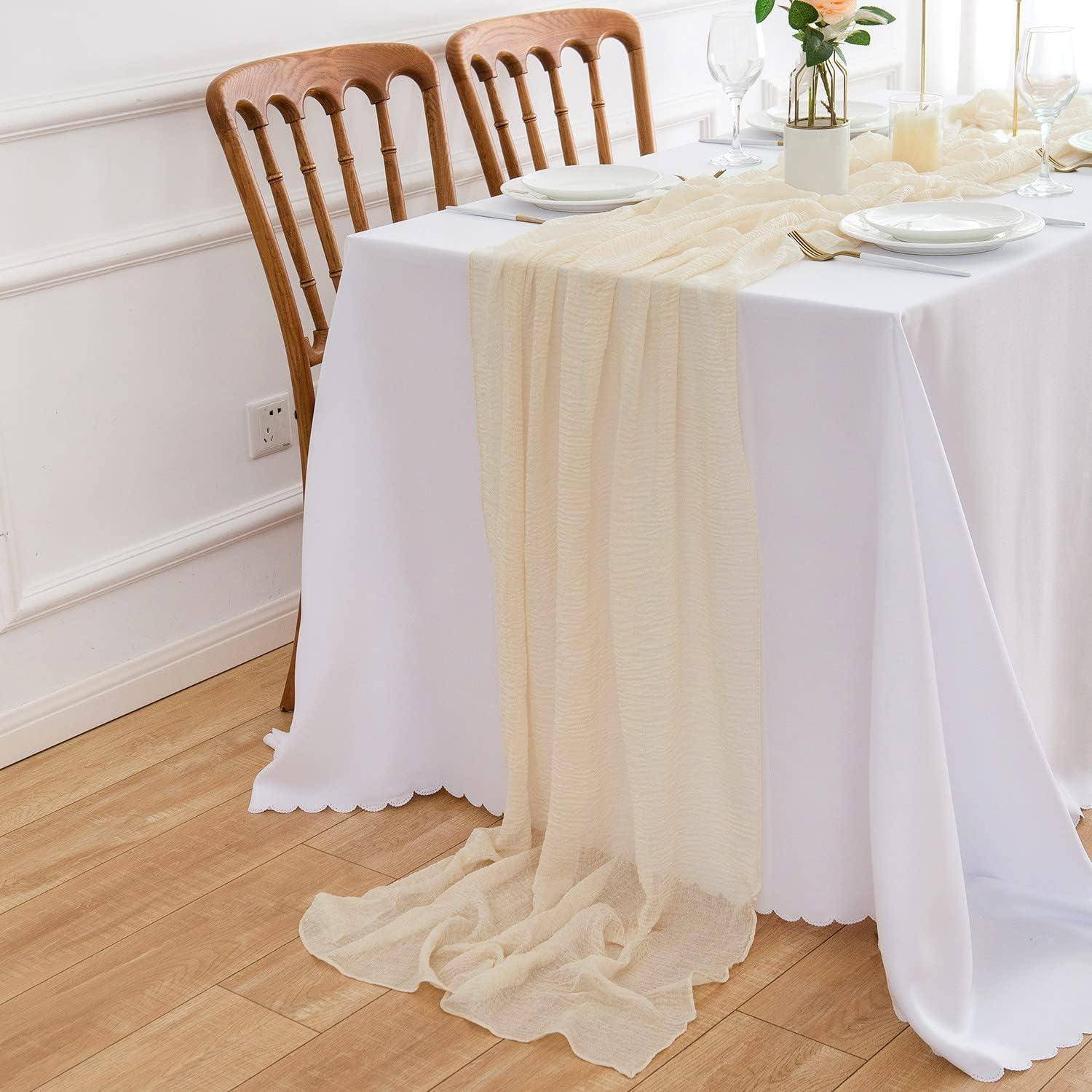 Ein weißer Tisch mit einem transparenten beigen Läufer und eleganten Gedecken, vor einer schlichten Inneneinrichtung mit Holzstühlen und hellem Holzboden.