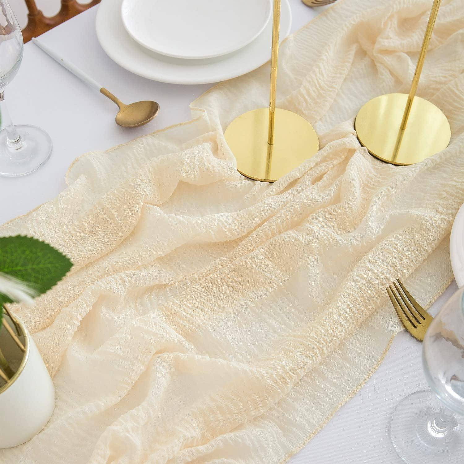 Eine cremefarbene Tischdecke mit goldenen Kerzenhaltern, weißen Tellern und Besteck, elegant auf einem Esstisch angeordnet.