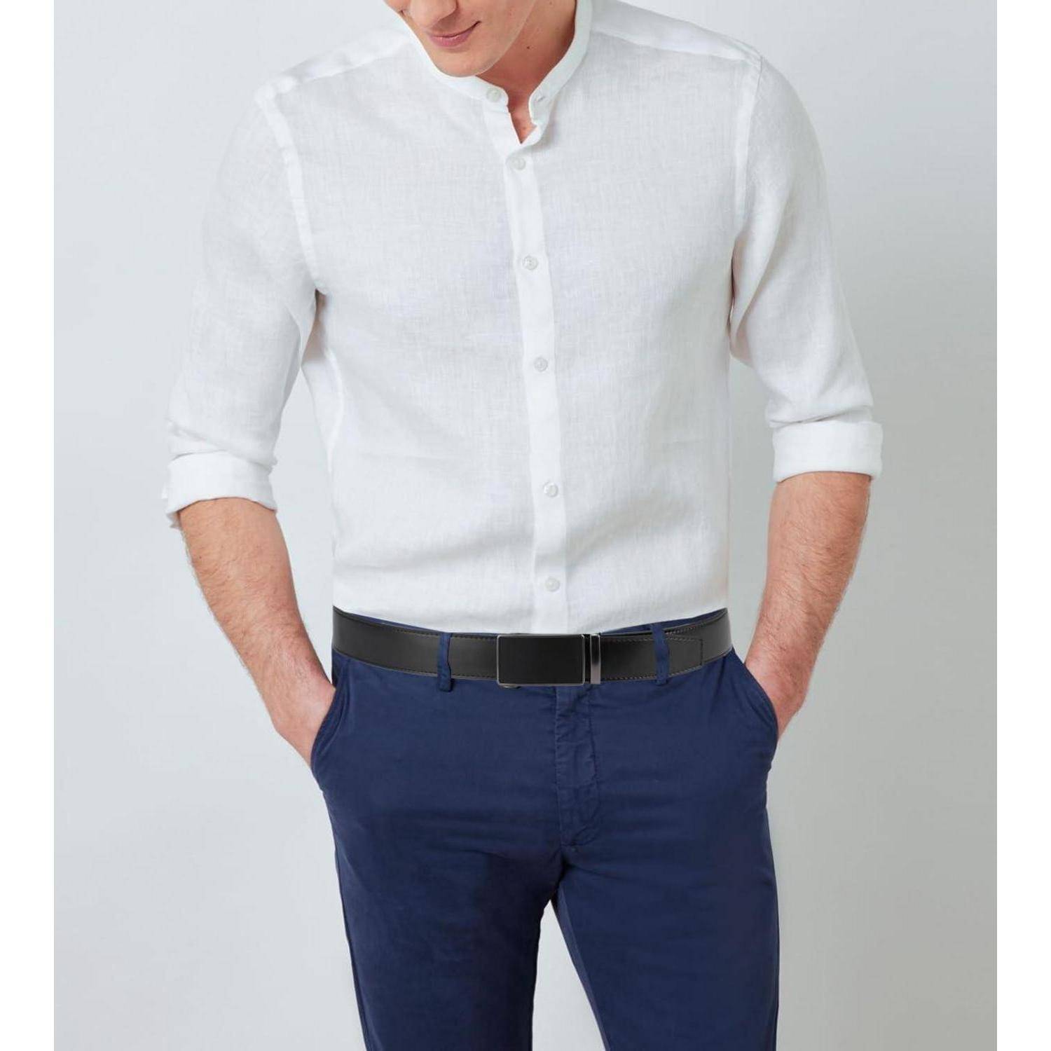 Eine Person in einem weißen Hemd mit hochgekrempelten Ärmeln und dunkelblauer Hose, die vor einem einfarbigen Hintergrund steht.