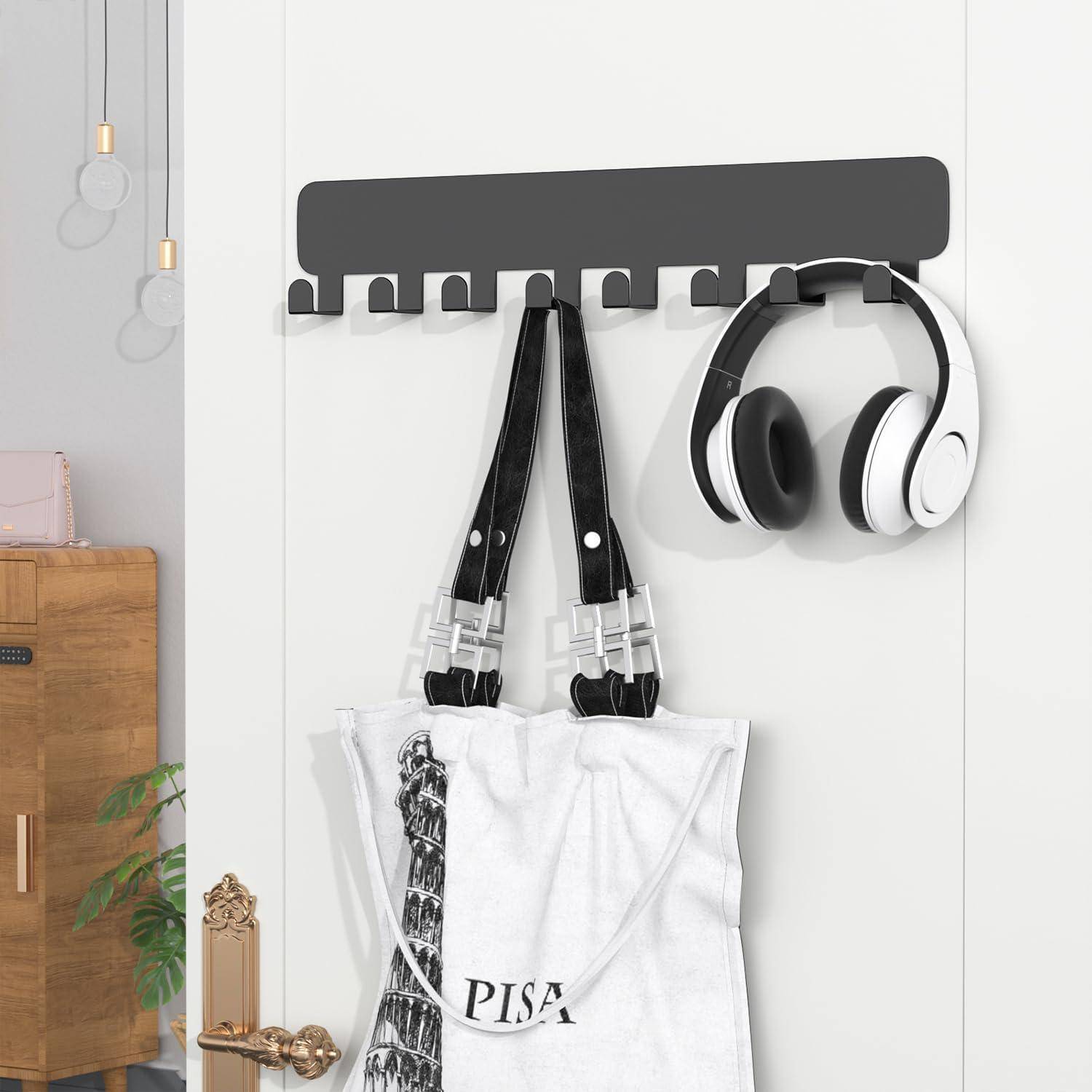 Kopfhörer und eine ‚PISA' Einkaufstasche, die an einem schwarzen Wandhaken über einer weißen Tür hängen, mit einem Holzschrank und Pflanzen in der Nähe.