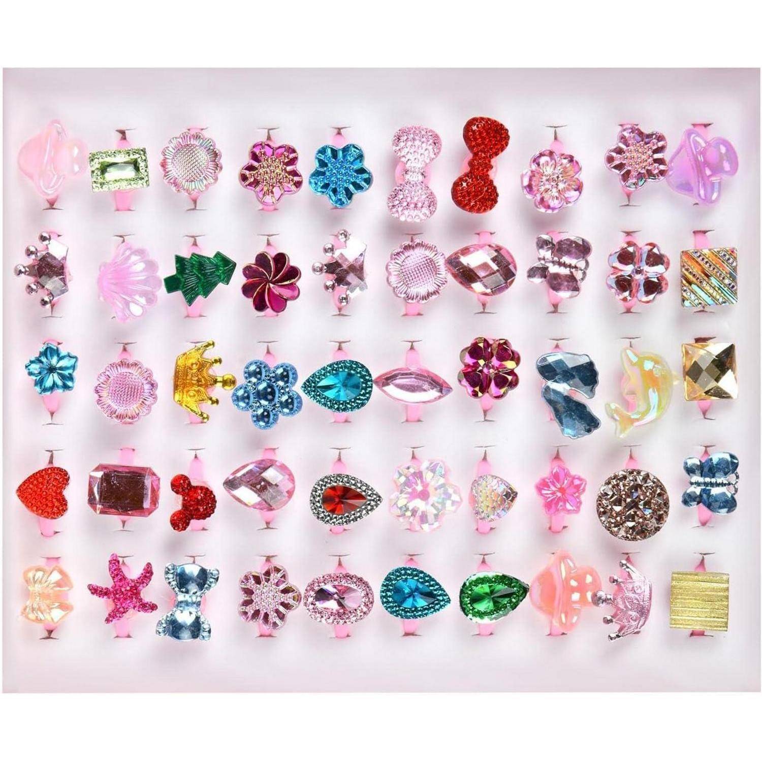 Eine Sammlung von bunten, dekorativen Ringen mit verschiedenen Designs und Mustern, die auf einem weichen rosa Hintergrund in einem organisierten Raster angeordnet sind.