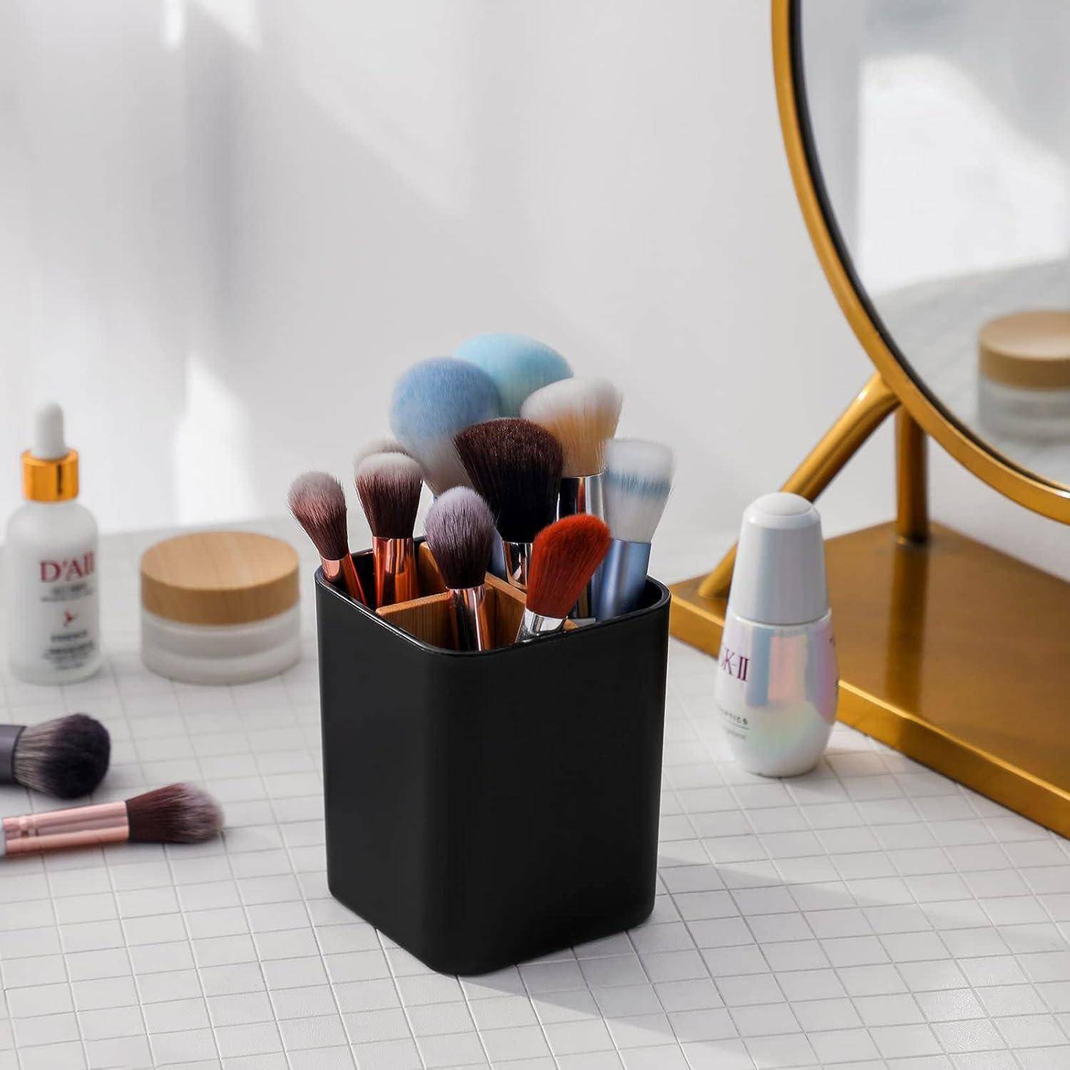 Ein Set verschiedener Make-up-Pinsel in einem schwarzen Halter auf einer weißen Oberfläche mit Gittermuster, daneben ein Spiegel und Hautpflegeprodukte.