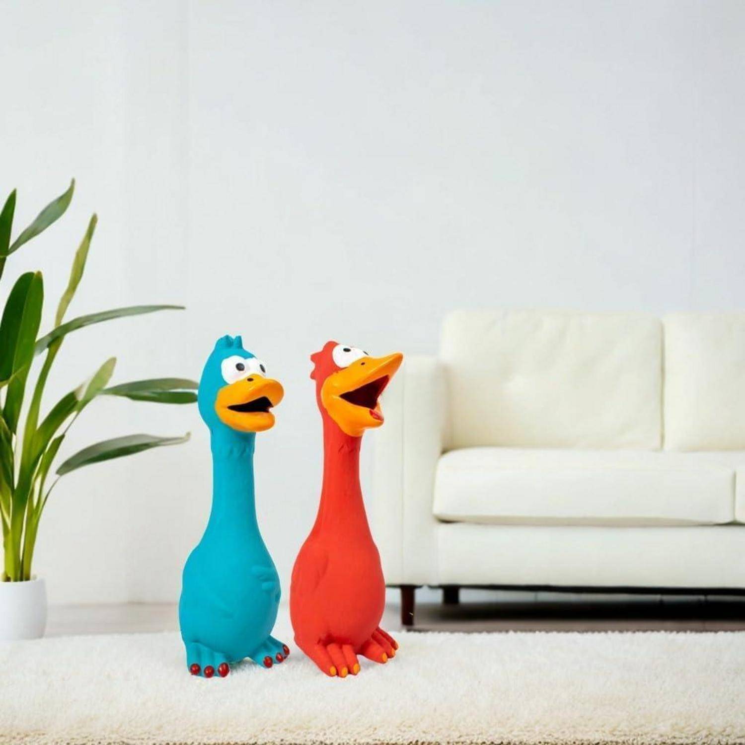 Zwei farbenfrohe Cartoon-Vogelfiguren, einer blau und einer rot, stehen auf einem Teppich in einem hellen Raum mit einer weißen Couch und einer Pflanze.