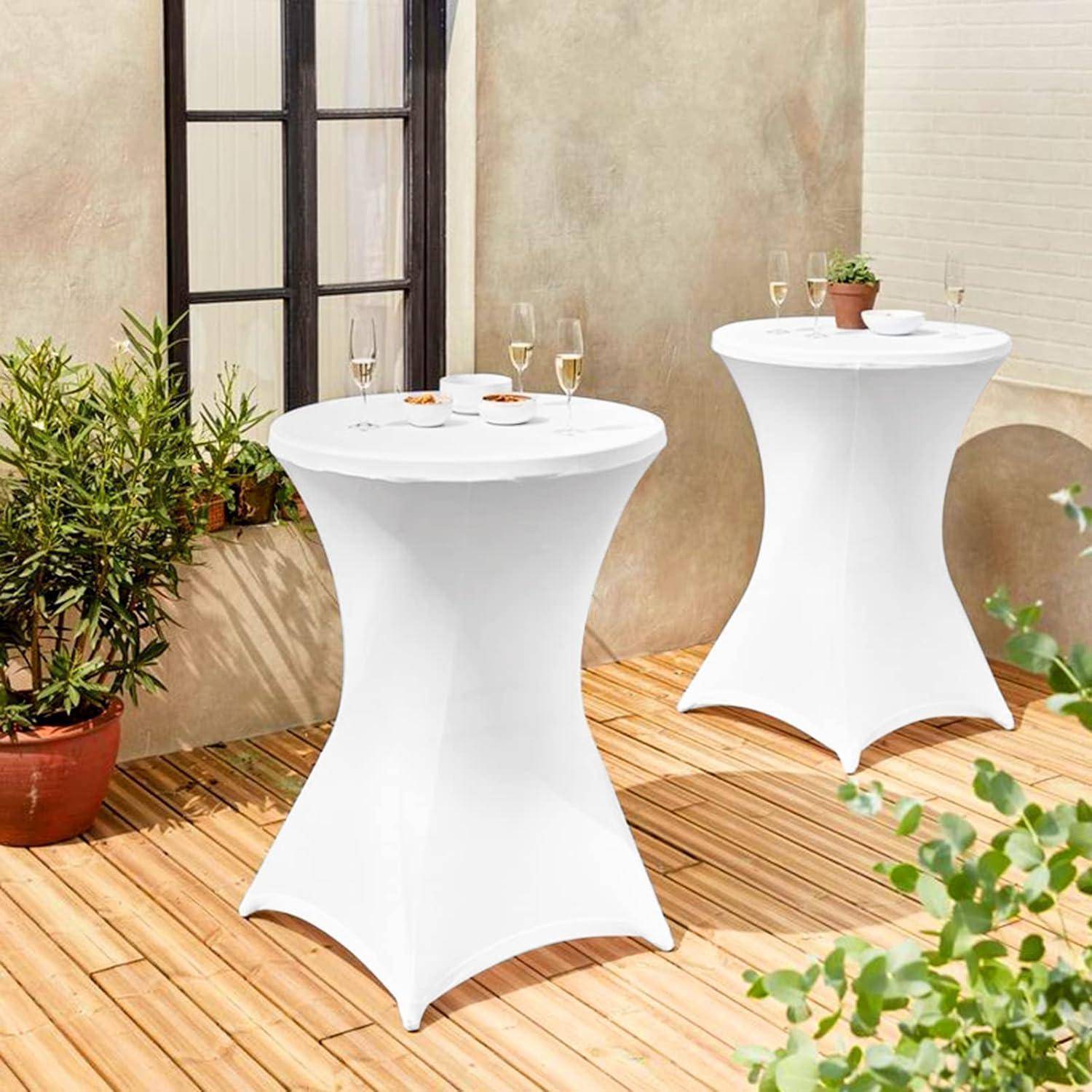 Zwei runde, weiß behangene Cocktailtische auf einer Holzterrasse, umgeben von Topfpflanzen. Auf einem Tisch stehen Weingläser und Teller.