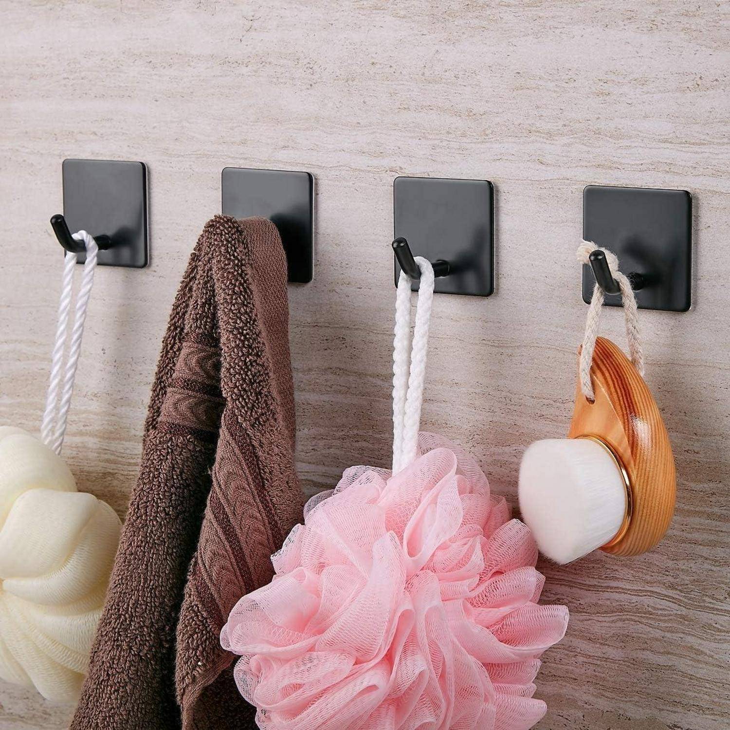 An der Wand befestigte Haken halten vier Baditems: einen gelben Luffa, ein braunes Handtuch, einen pinken Badeschwamm und eine Holzkörperbürste.