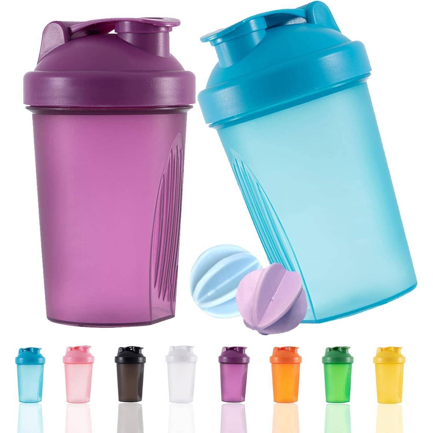 Zwei Shakerflasche, eine in Lila und eine in Blau, mit passenden Mischkugeln. Darunter sind kleinere Flaschen in verschiedenen Farben platziert.