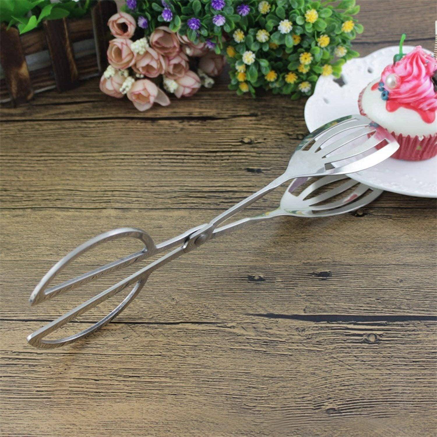 Ein Paar silberne Zangen auf einem Holztisch, neben einem Teller mit einem Cupcake, der mit weißer Buttercreme und einer pinken Dekoration verziert ist, umgeben von Blumen.