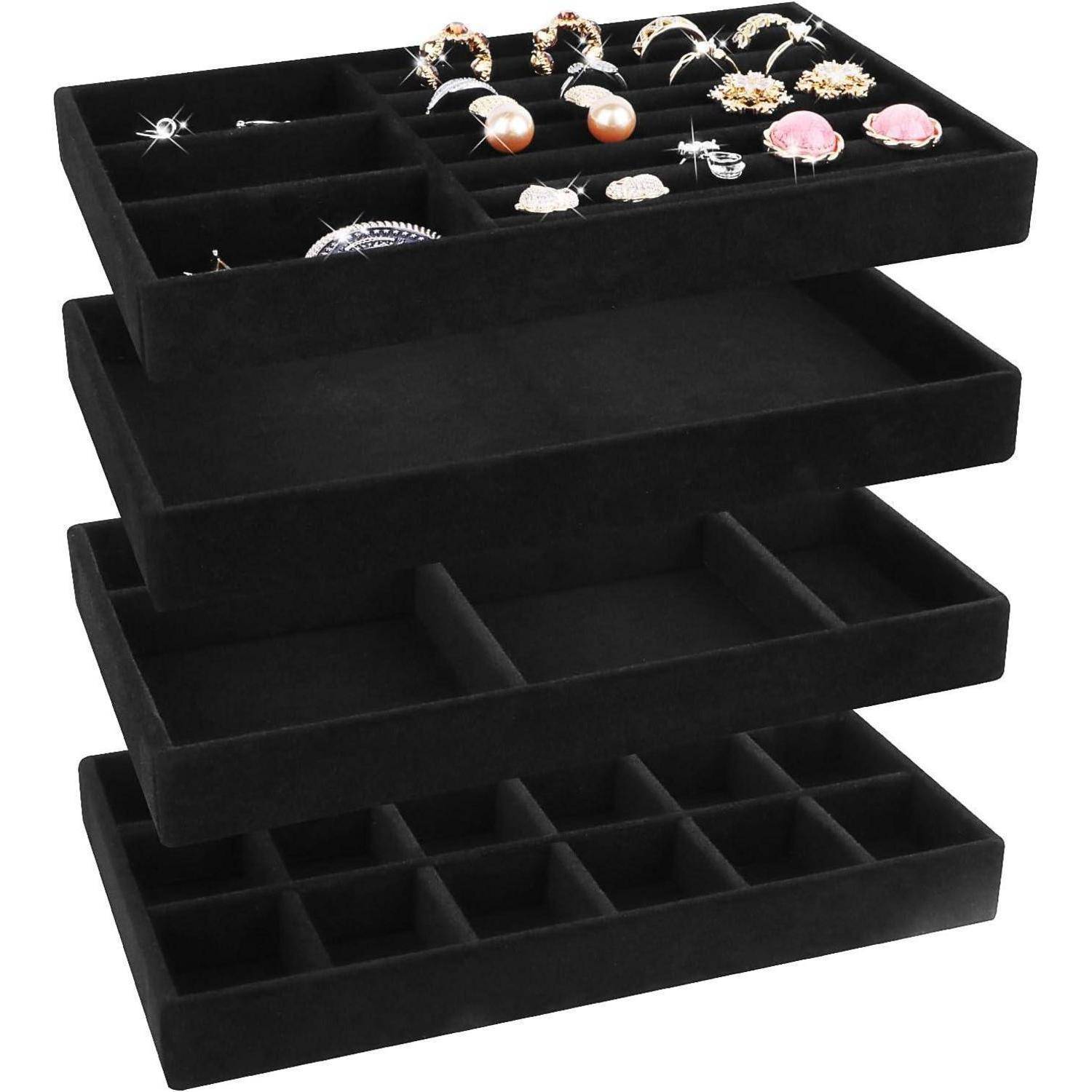 Ein Stapel von vier schwarzen Samtkassetten für Schmuck; die oberste Ablage zeigt Ringe und Ohrringe, während die anderen Tabletts leere Fächer haben.
