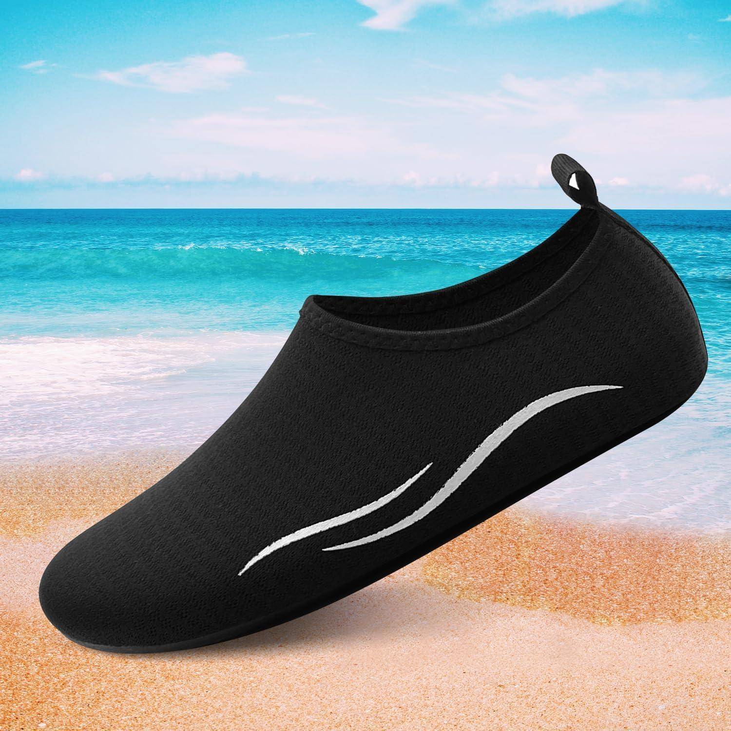 Ein schwarzer Wasserschuh mit weißem Swoosh-Design sitzt auf einem sandigen Strand mit dem Ozean und dem blauen Himmel im Hintergrund.