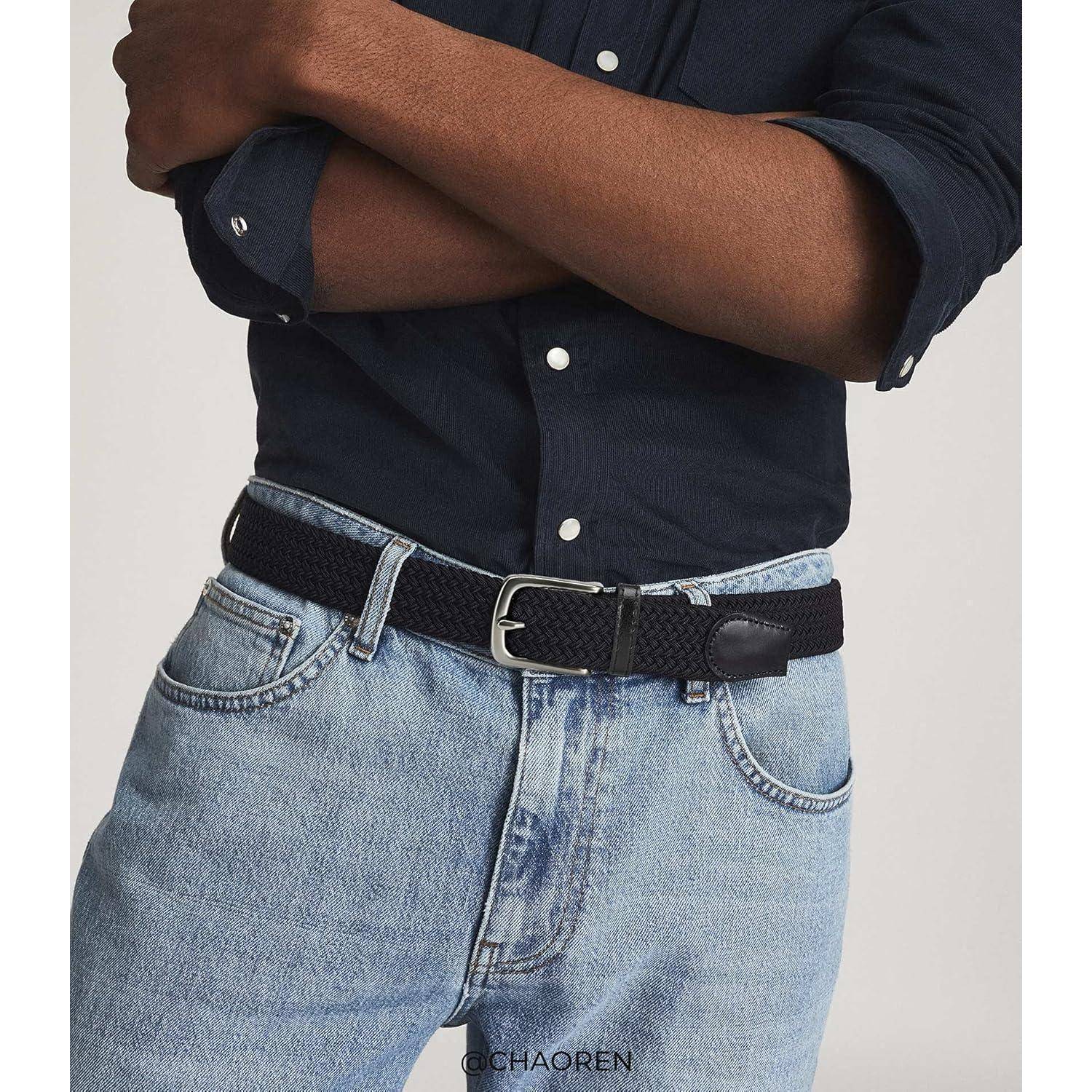 Eine Person mit einem dunklen Shirt und hellen Jeans, dazu einen schwarzen geflochtenen Gürtel, die Hände über der Brust verschränkt, was einen lässigen Stil betont.