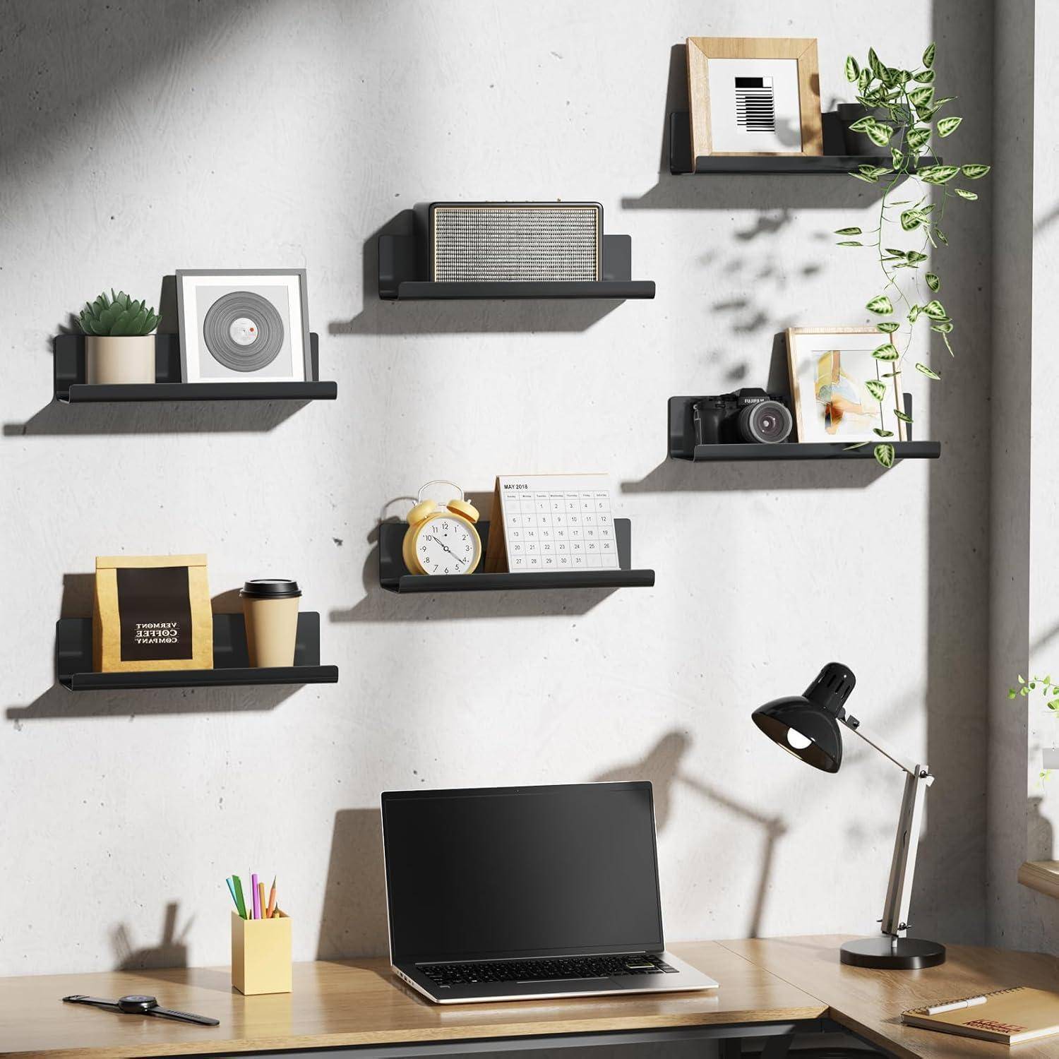 Ein aufgeräumter Schreibtisch im Home Office mit einem Laptop, einer Lampe und einem Stiftehalter. Schwarze Regale an der Wand tragen Bücher, Pflanzen, eine Kamera und Dekorationsgegenstände.