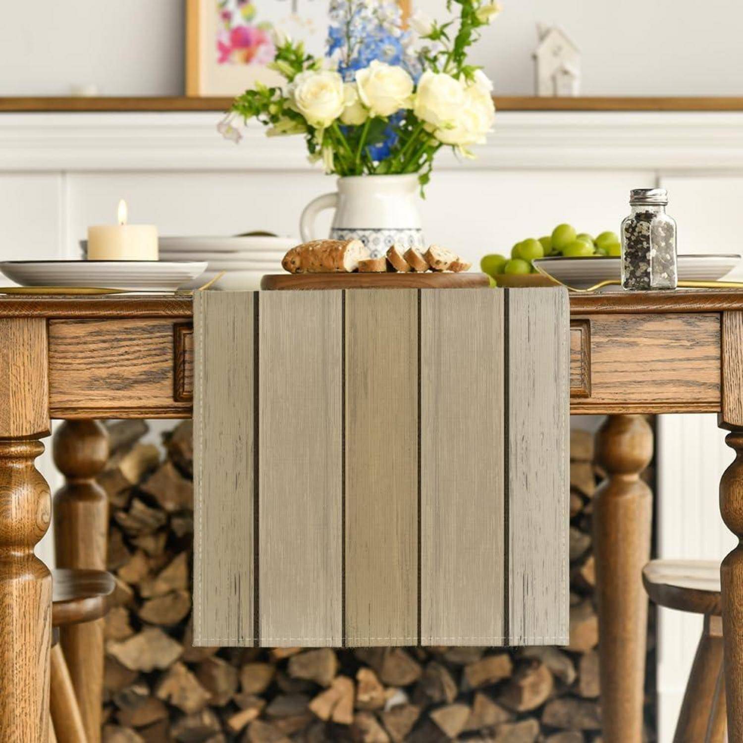 Ein rustikaler Holztisch mit einem neutralen Tischläufer ist mit einer Kerze, Brot und einem Blumenarrangement als Tischdekoration gedeckt. Brennholz wird darunter gelagert.