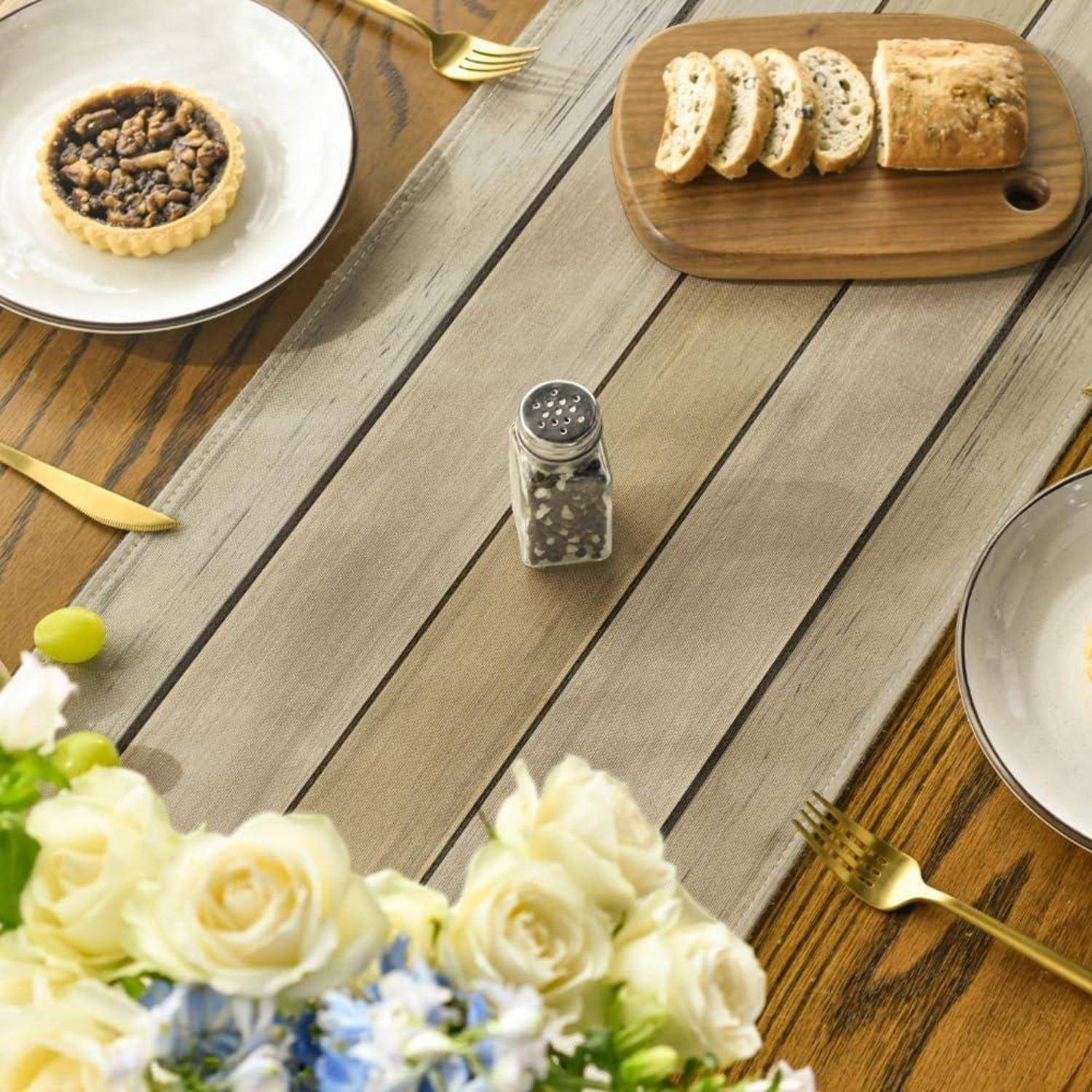 Ein Esstisch, gedeckt für eine Mahlzeit mit einer Pastete, Brotscheiben und einer Pfeffermühle, umgeben von goldenem Besteck und einem Blumenarrangement im Vordergrund.