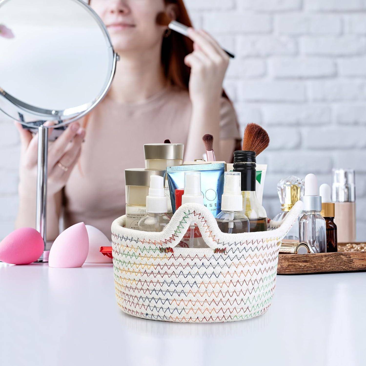 Eine Person trägt Make-up auf, während sie einen Spiegel hält, umgeben von Beautyprodukten in einem Korb und auf einem Tisch, was auf eine persönliche Pflegeroutine hindeutet.