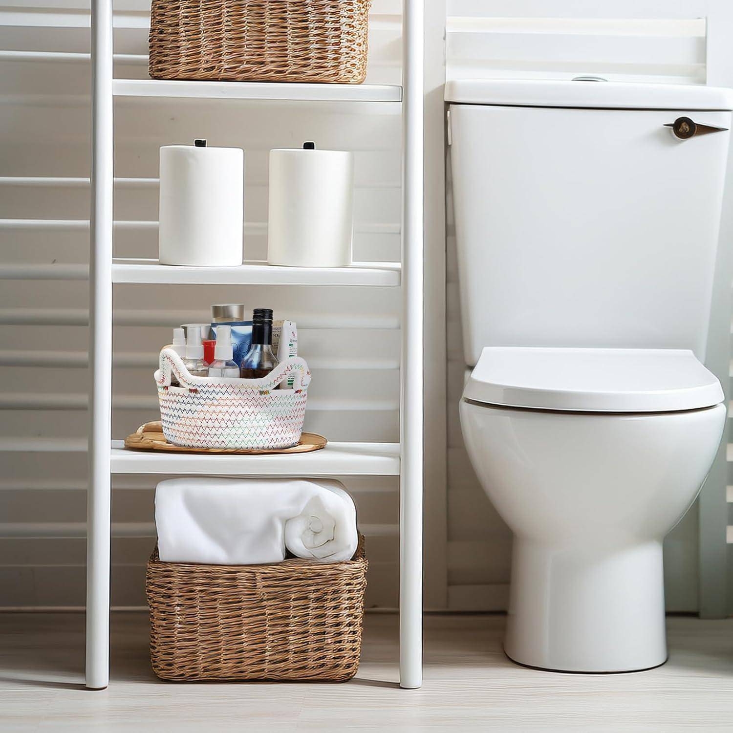Badezimmerszene mit einer Toilette und einem weißen Regal, das Toilettenpapier, Toilettenartikel in einem Korb und ein zusammengerolltes Handtuch neben einem Fenster enthält.