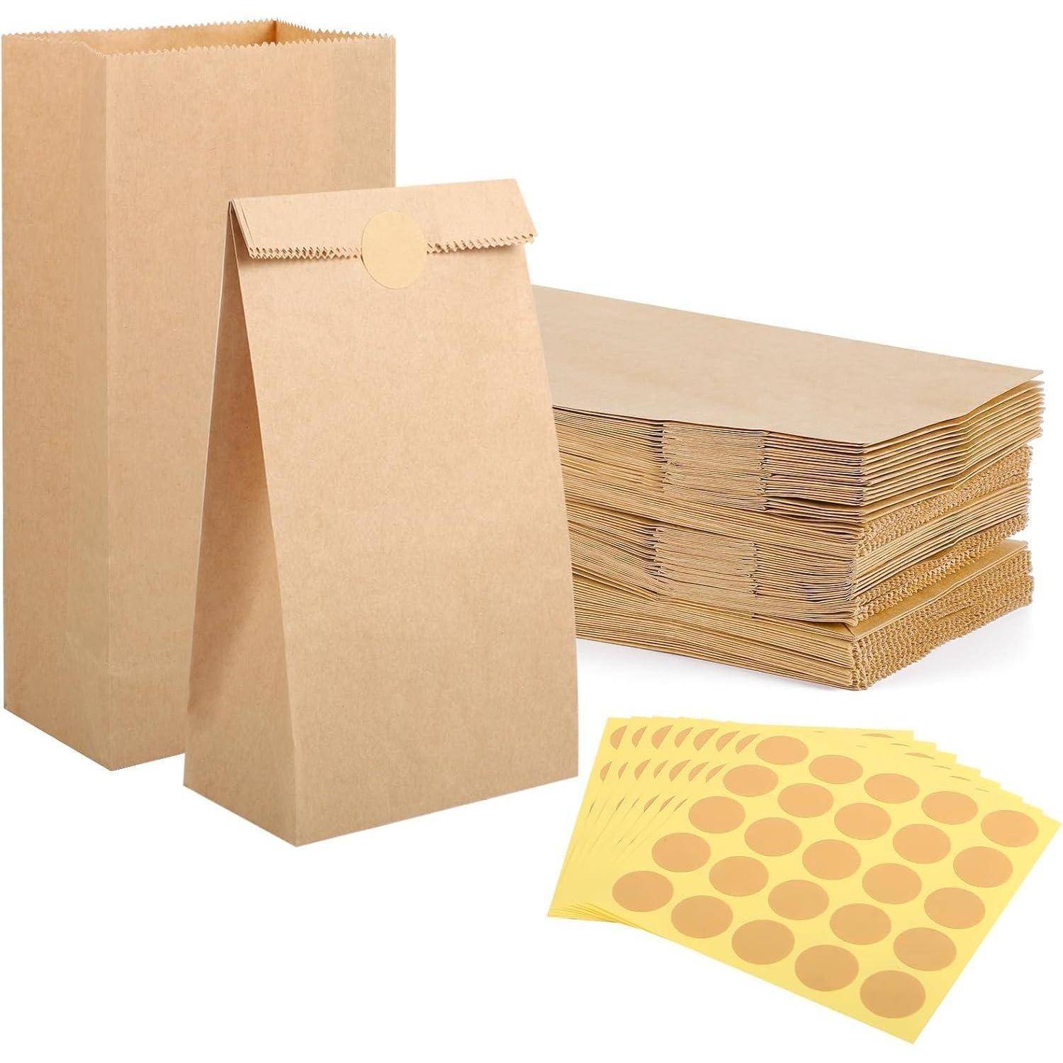 Ein Stapel brauner Papiertüten, eine geschlossene Tüte aufrecht stehend, und Blätter mit runden gelben Aufklebern, was auf Verpackung oder Geschenkherstellung hindeutet.