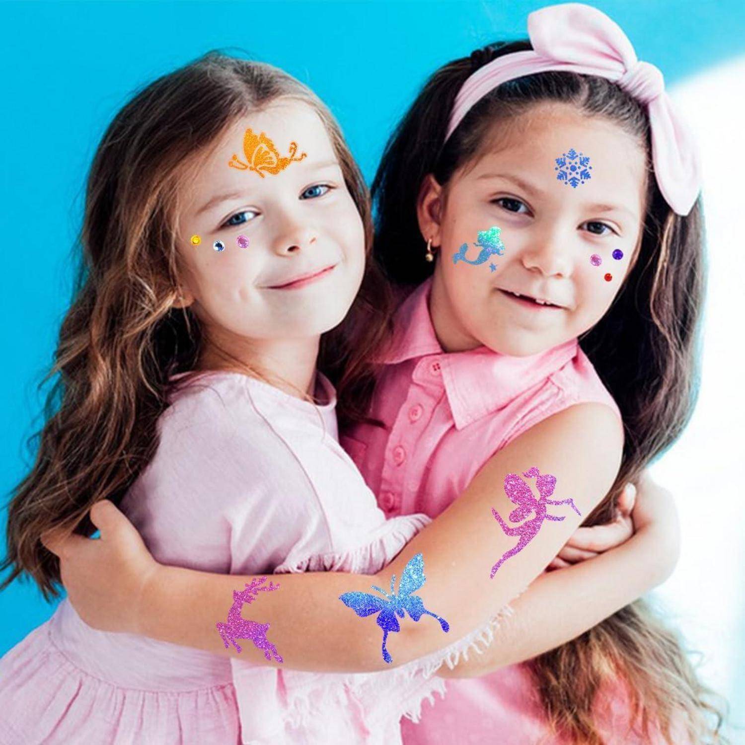 Zwei junge Mädchen lächeln und umarmen sich gegenseitig und tragen glitzernde Gesichts- und Armtattoos von Schmetterlingen, Feen und anderen bunten Designs.