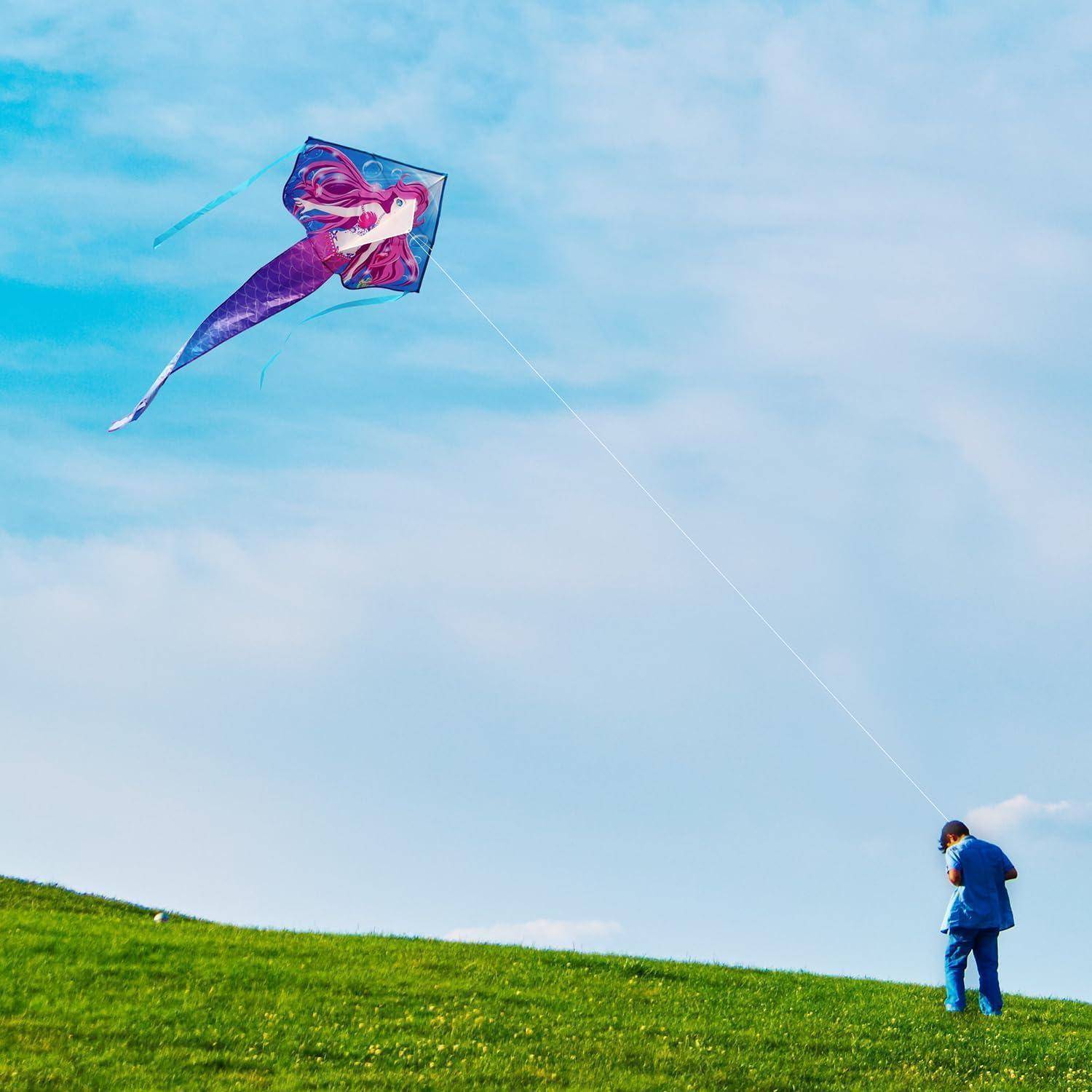 Eine Person, die auf einem grasigen Hügel steht und einen bunten Drachen in einem blauen Himmel fliegt.