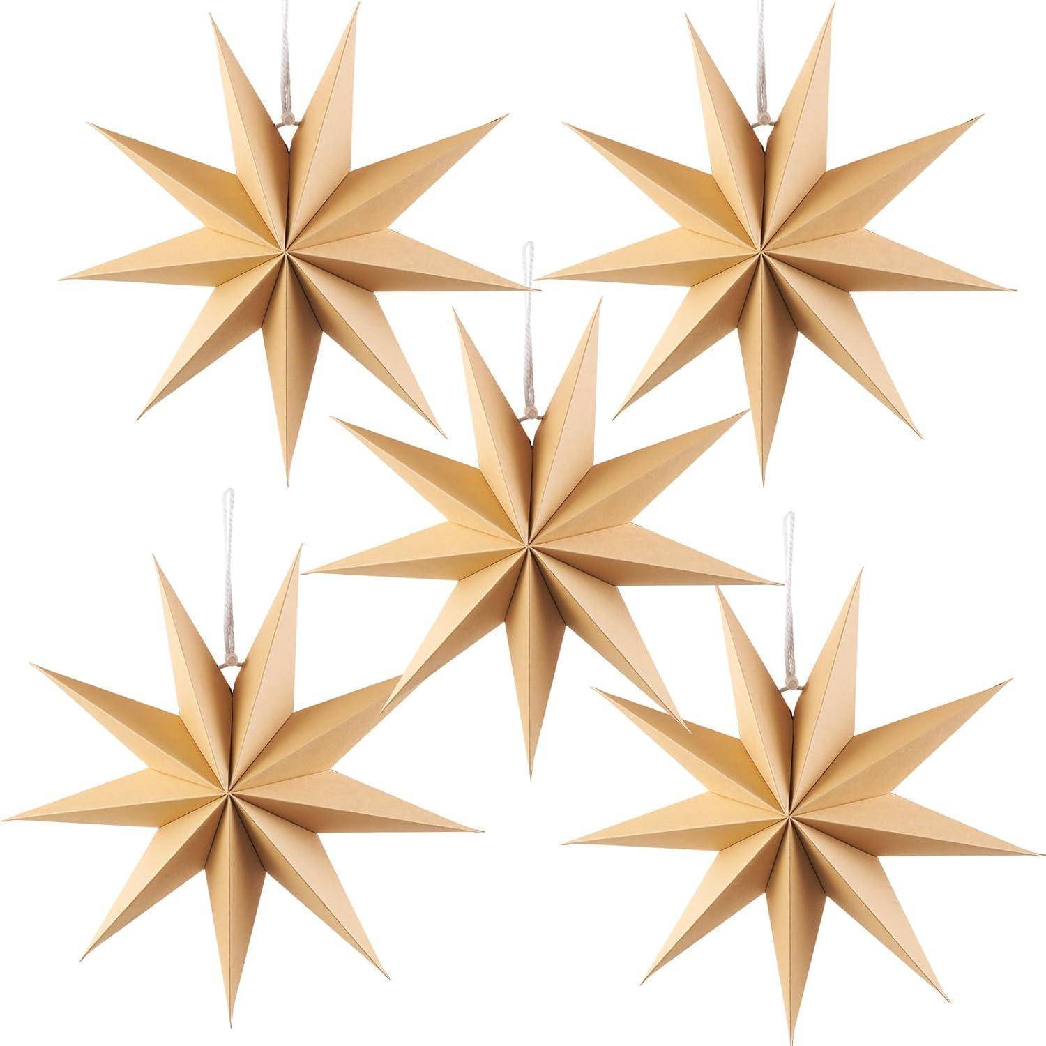 Fünf beige, dreidimensionale Papiersterne mit spitzen Spitzen, an Schnüren hängend, symmetrisch vor einem weißen Hintergrund angeordnet.