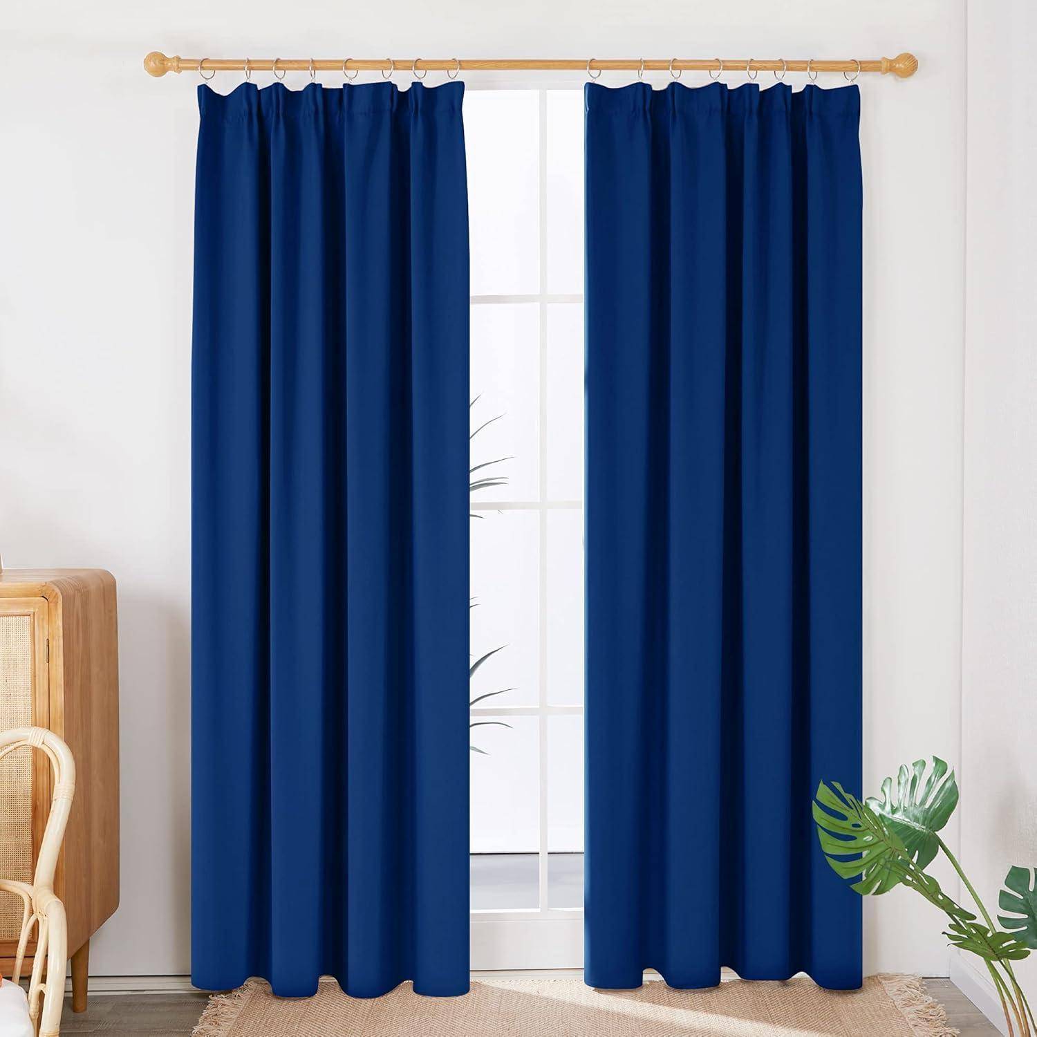 Blaue Vorhänge hängen an einem Fenster und verdecken teilweise den Blick auf Zimmerpflanzen. Ein Holzschrank ist links sichtbar.