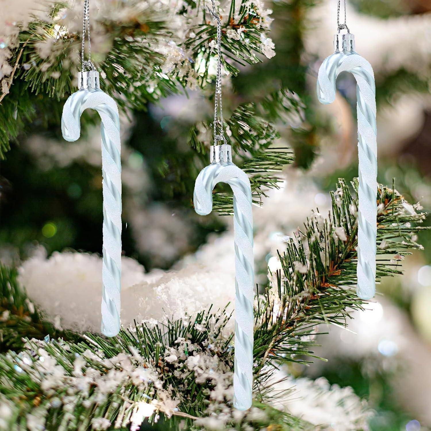 Drei weiße Zuckerstangenornamente hängen an einem Weihnachtsbaum mit grünen Zweigen und weißen Schneeakzenten.