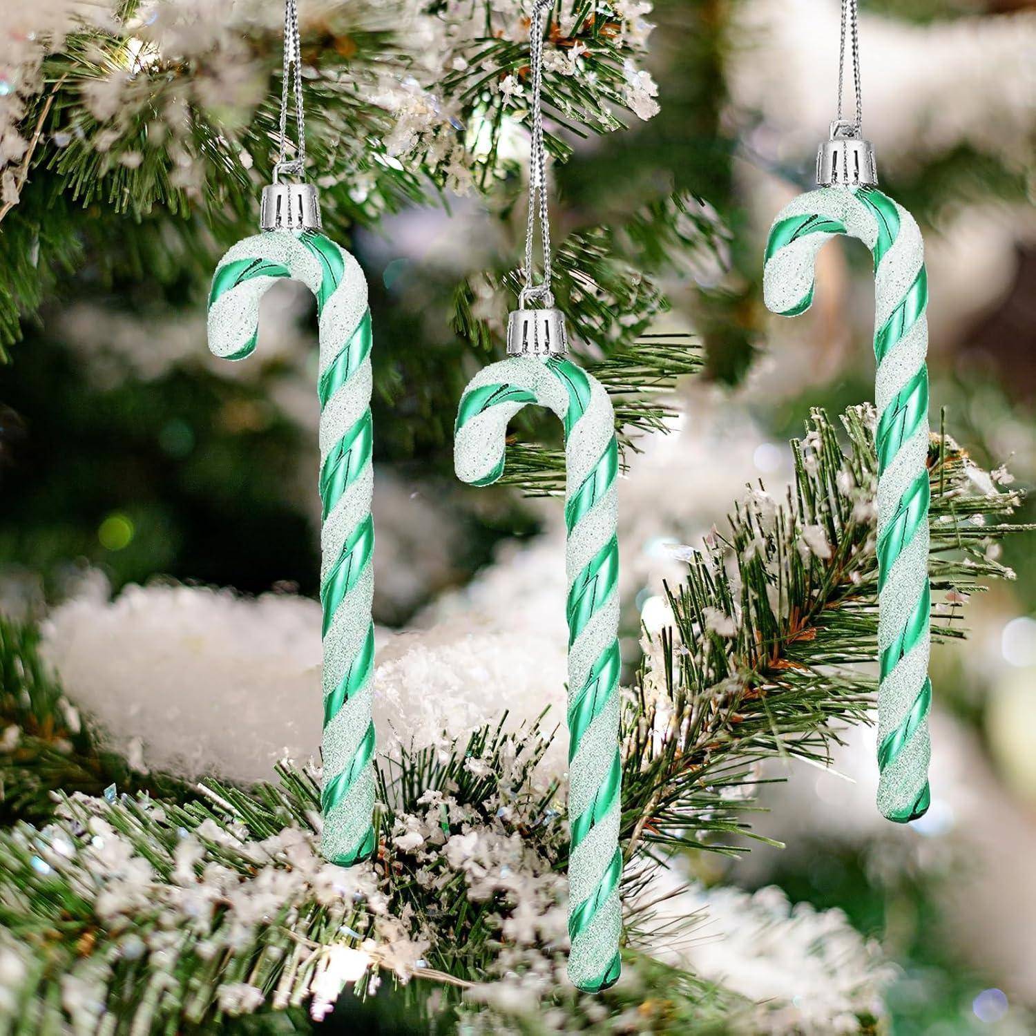 Drei grün-weiß gestreifte Zuckerstangen-Anhänger hängen an schneebedeckten Zweigen eines Weihnachtsbaums.