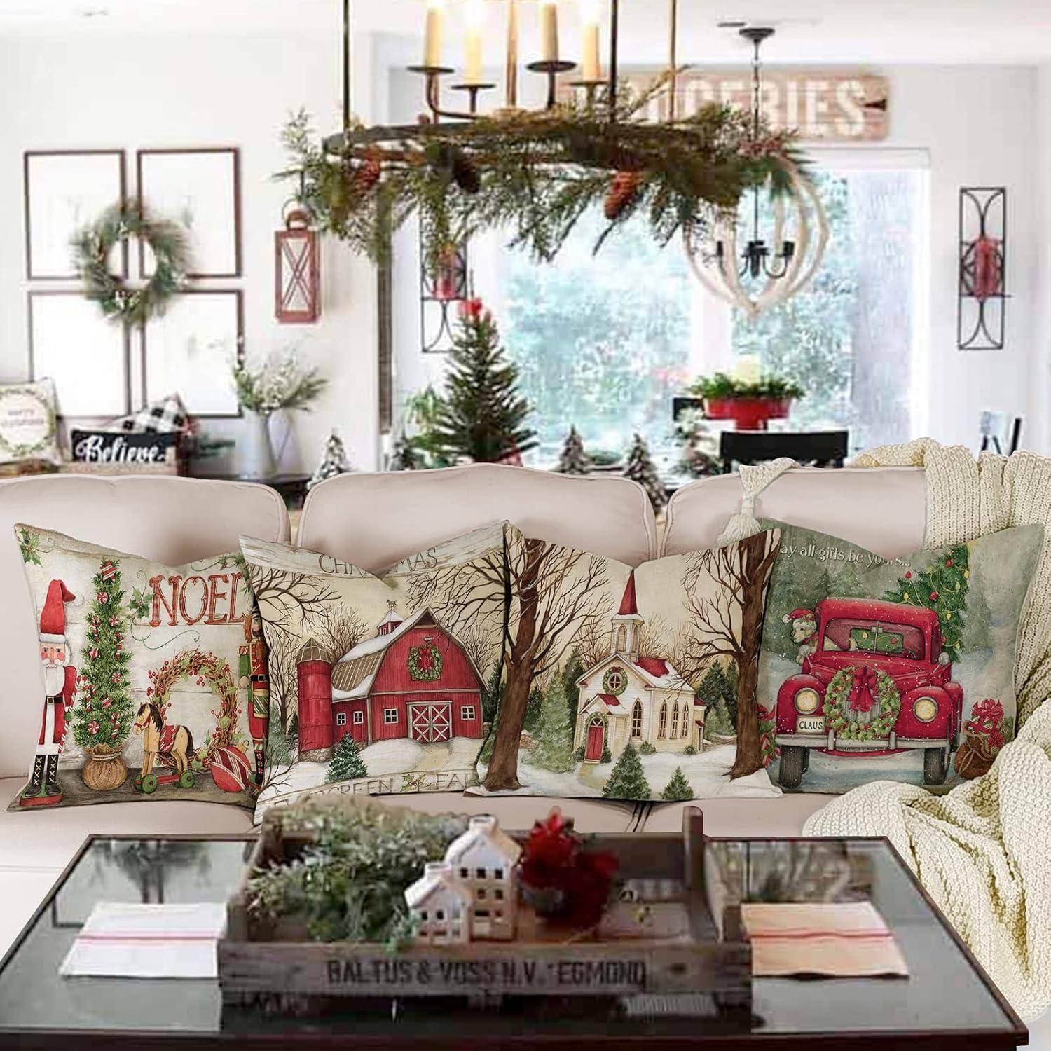 Ein gemütliches Wohnzimmer, weihnachtlich dekoriert mit festlichen Kissen, die Feiertagsszenen zeigen, und einem roten Truck. Ein Kronleuchter mit Grünzeug hängt darüber.