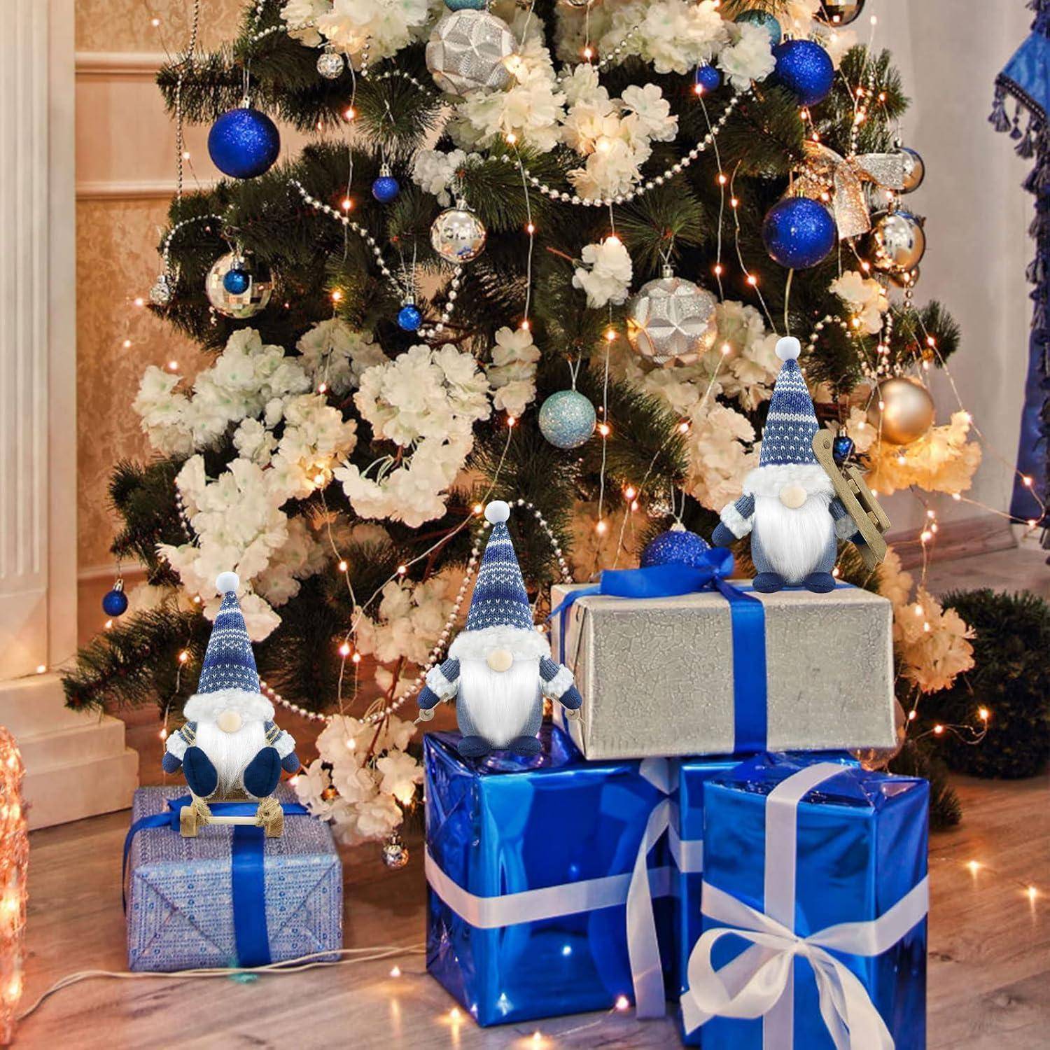 Ein festlich geschmückter Weihnachtsbaum mit blauen und weißen Christbaumkugeln und Lichtern steht hinter blau eingepackten Geschenken, die mit Wichtelfiguren verziert sind.