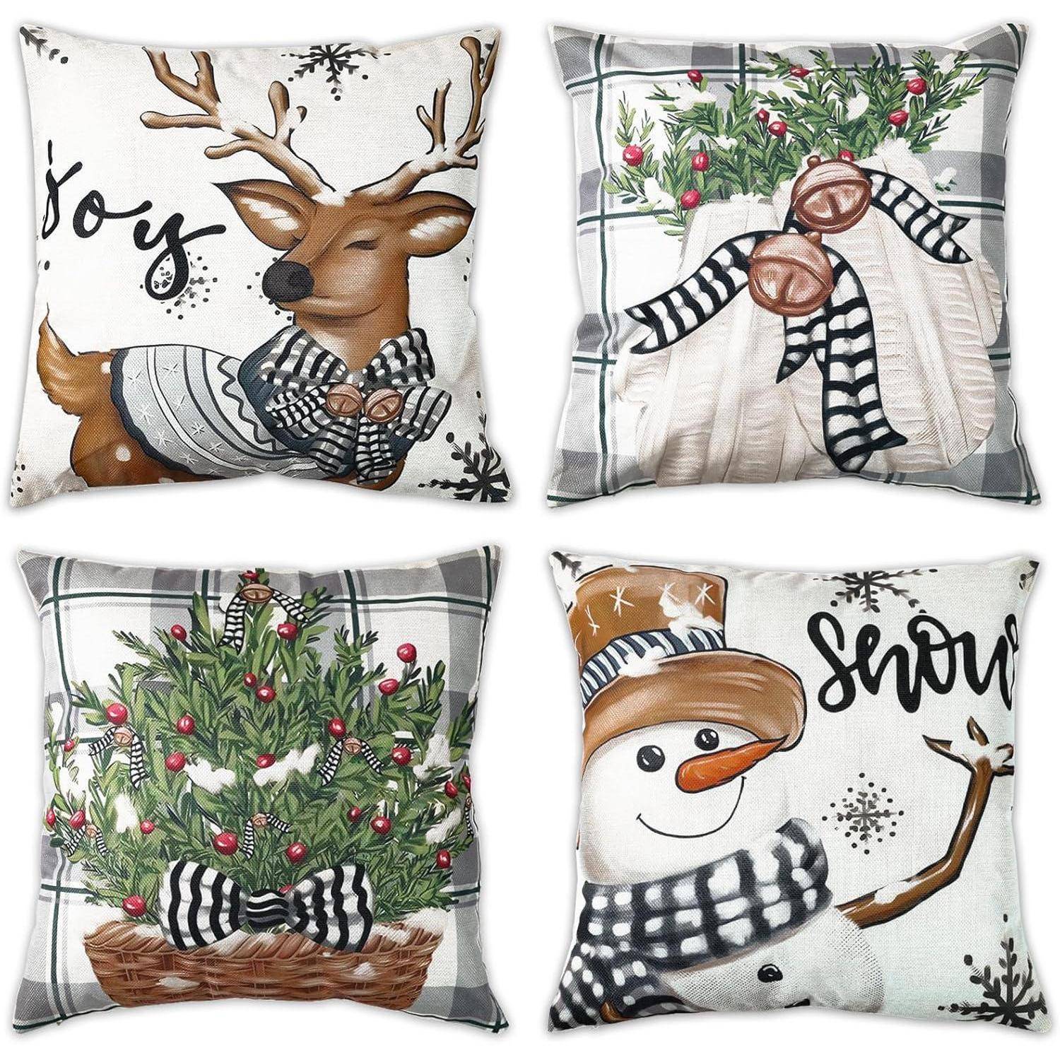 Vier festliche Kissen mit weihnachtlichen Motiven: ein Rentier mit der Aufschrift 'Freude', Handschuhe und Grünzeug, ein geschmückter Baum und ein Schneemann mit der Aufschrift 'Schnee'.