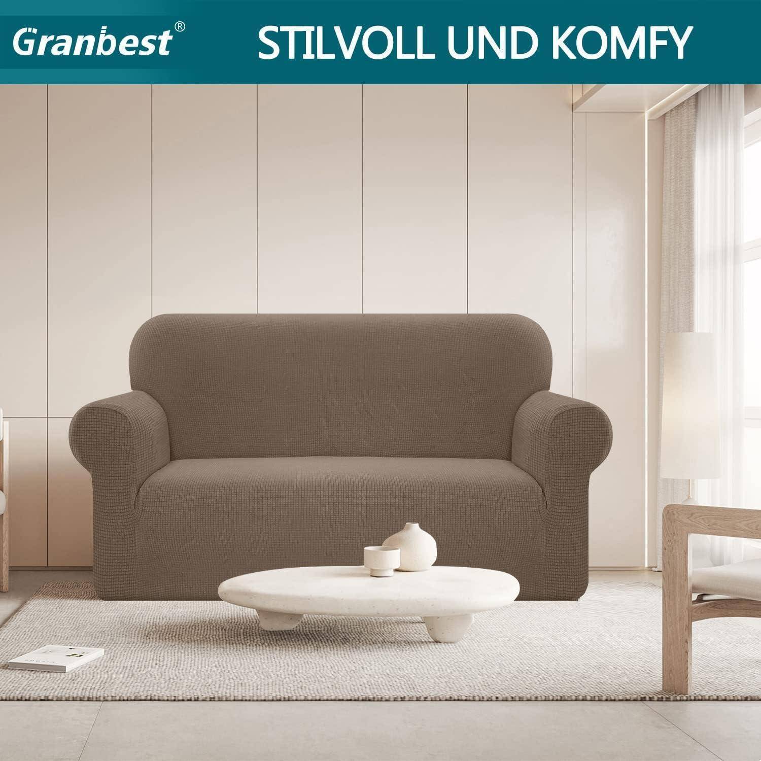 Ein Wohnzimmer mit einem grauen Sofa, das mit einem dehnbaren Stoffbezug überzogen ist, einem runden weißen Couchtisch und natürlichem Licht von einem großen Fenster.