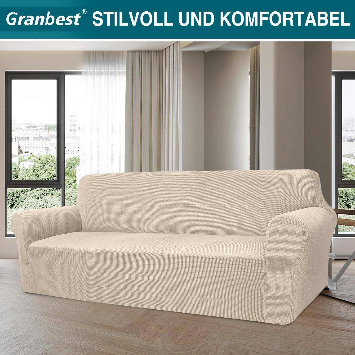 Ein beiger Sofabezug auf einem Sofa in einem modernen Wohnzimmer mit großen Fenstern. Der Text oben liest sich: 