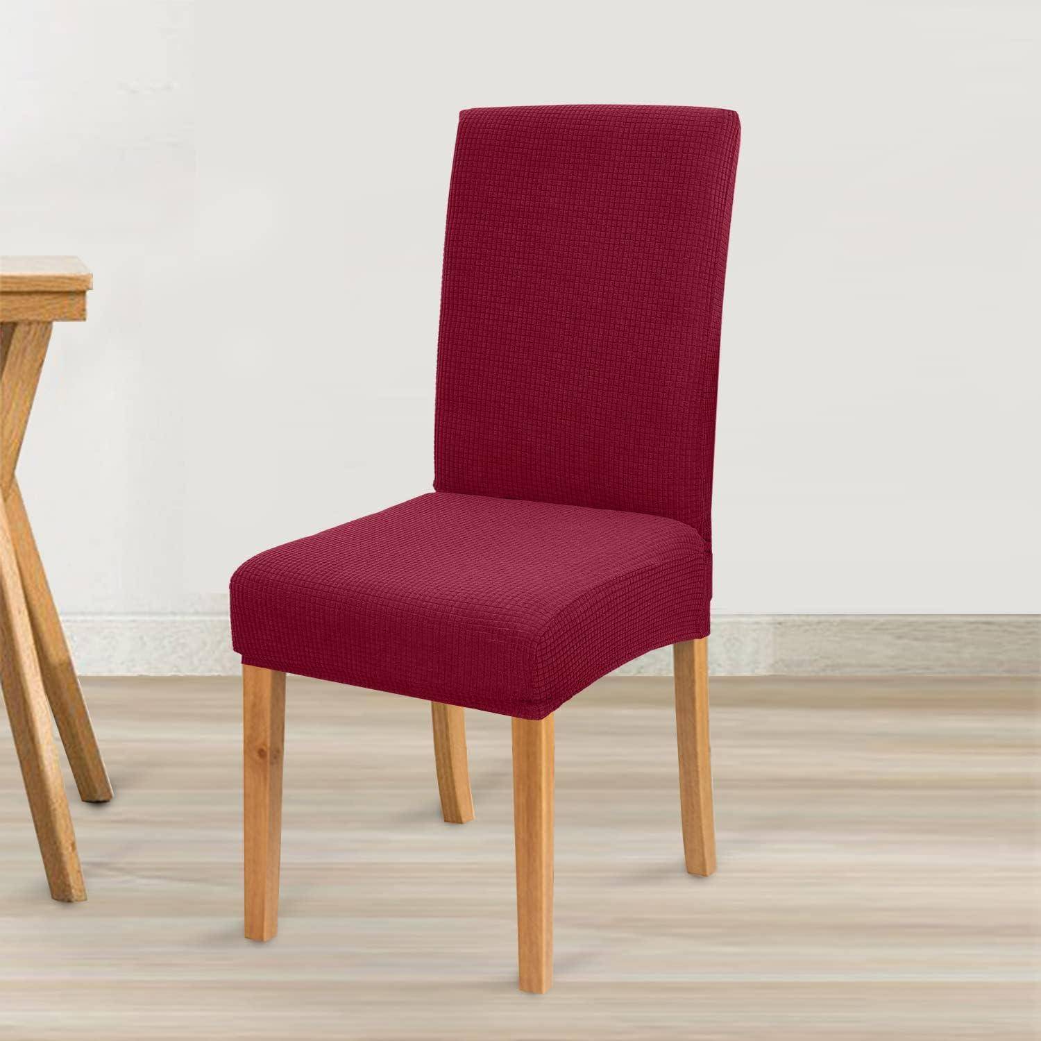 Ein roter gepolsterter Essstuhl mit Holzbeinen steht auf einem hellen Holzboden neben einer Ecke eines Holztisches vor einer einfarbigen Wand.