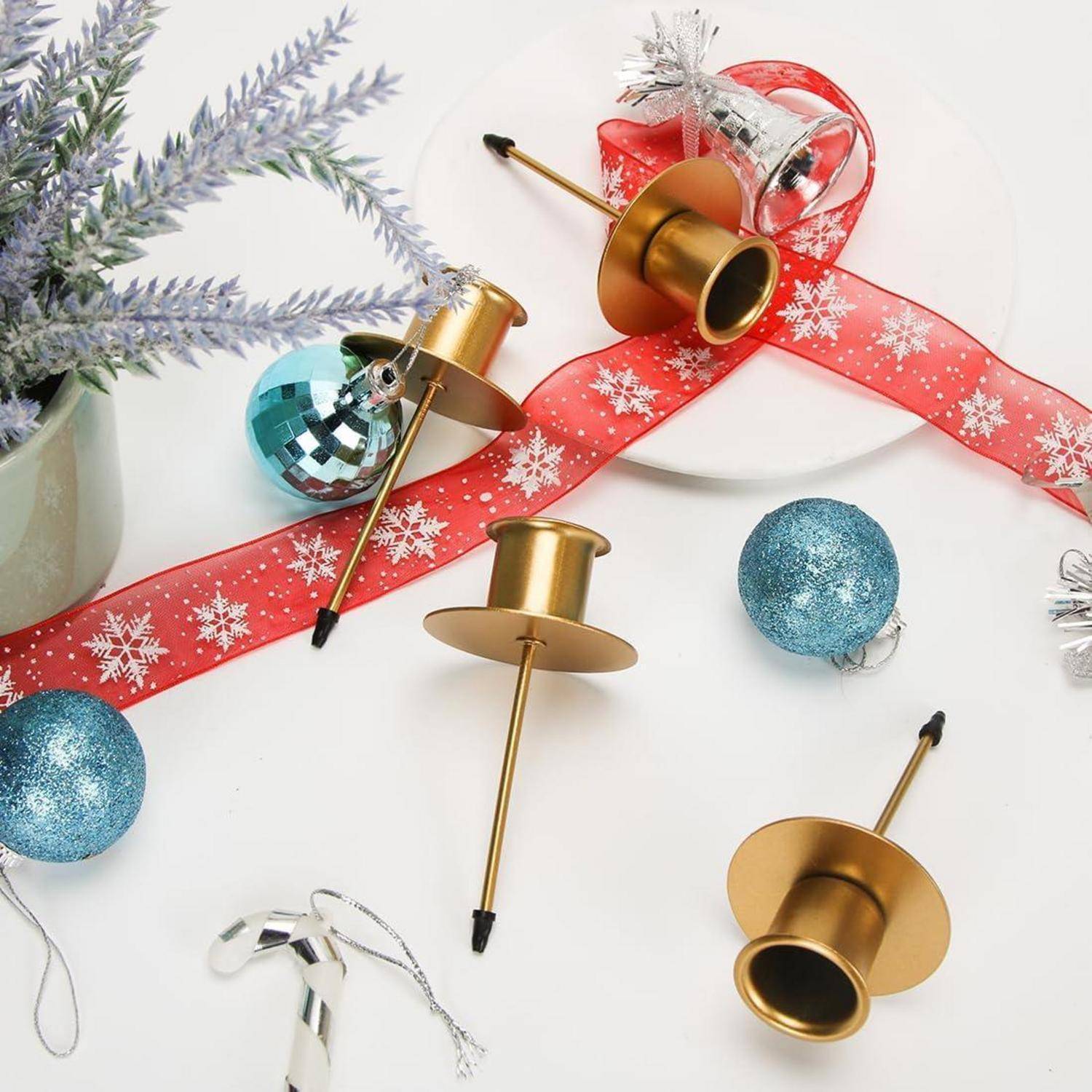 Goldene Kerzenhalter, blaue Christbaumkugeln und rotes Band mit Schneeflockenmustern sind auf einer weißen Oberfläche für eine festliche Dekoration angeordnet.