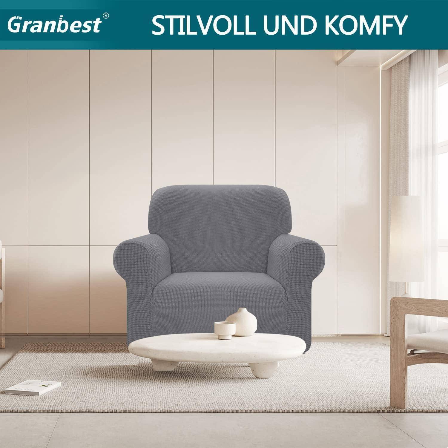 Ein grauer Sessel in einem modernen Wohnzimmer mit beigen Wänden. Ein runder Couchtisch mit einer weißen Vase steht davor. Text lautet: 