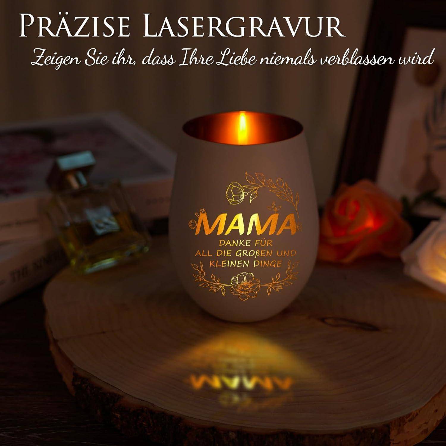 Ein Kerzenhalter mit dem Wort 'Mama' und dem Text 'Danke für all die großen und kleinen Dinge', beleuchtet von einer Flamme und umgeben von Dekoration.