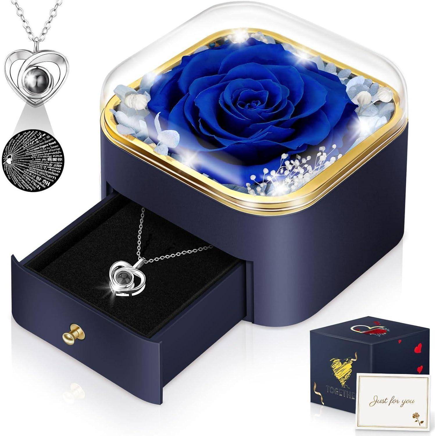 Eine blaue Rose, eingeschlossen in einer durchsichtigen Schachtel mit goldenem Rand; darunter eine offene Schublade mit einer herz-förmigen Anhängerkette. Eine kleine Karte trägt die Aufschrift „Nur für dich
