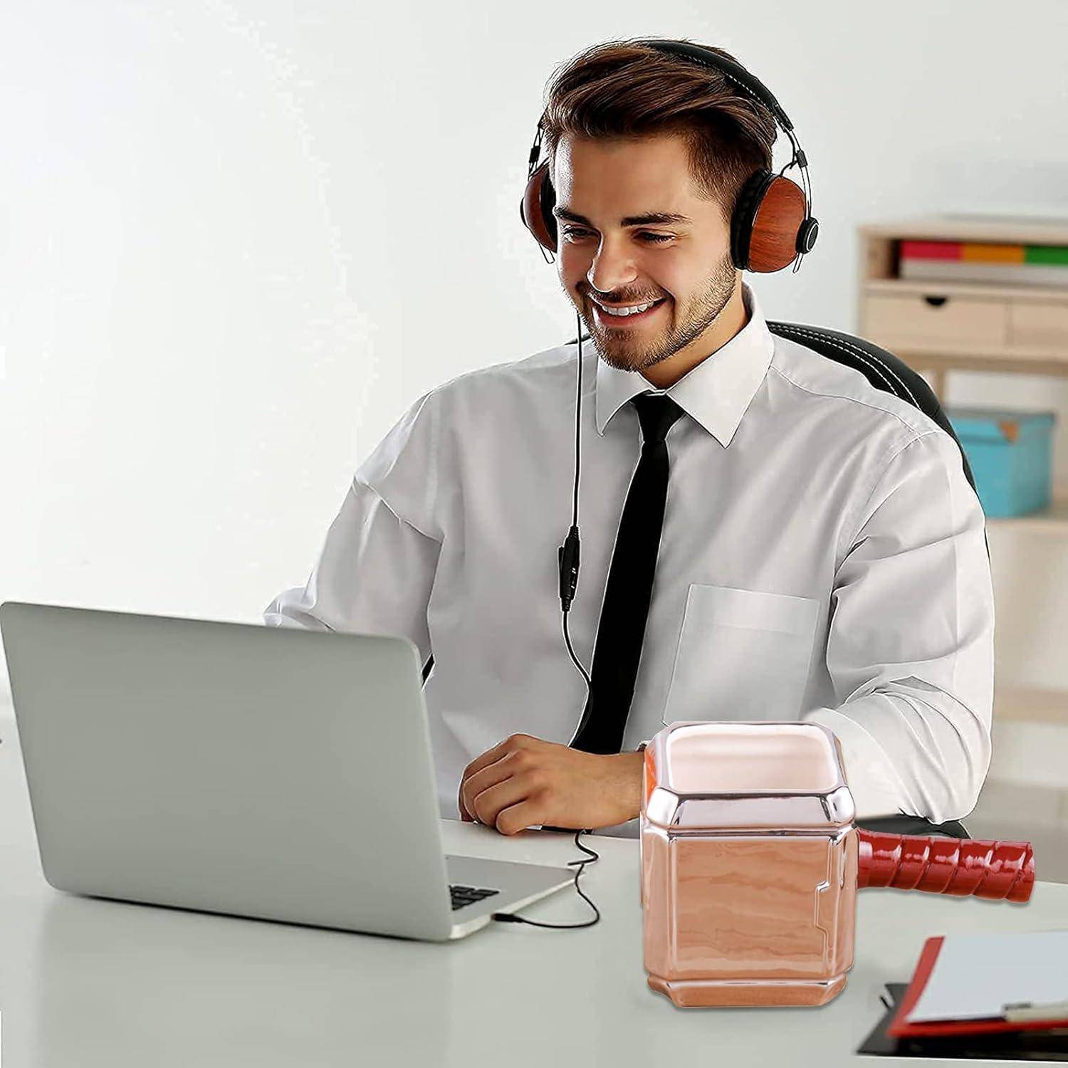Eine Person in einem weißen Hemd und Krawatte lächelt, während sie Kopfhörer trägt und einen Laptop benutzt. Eine Parfümflasche ist auf dem Schreibtisch zu sehen.