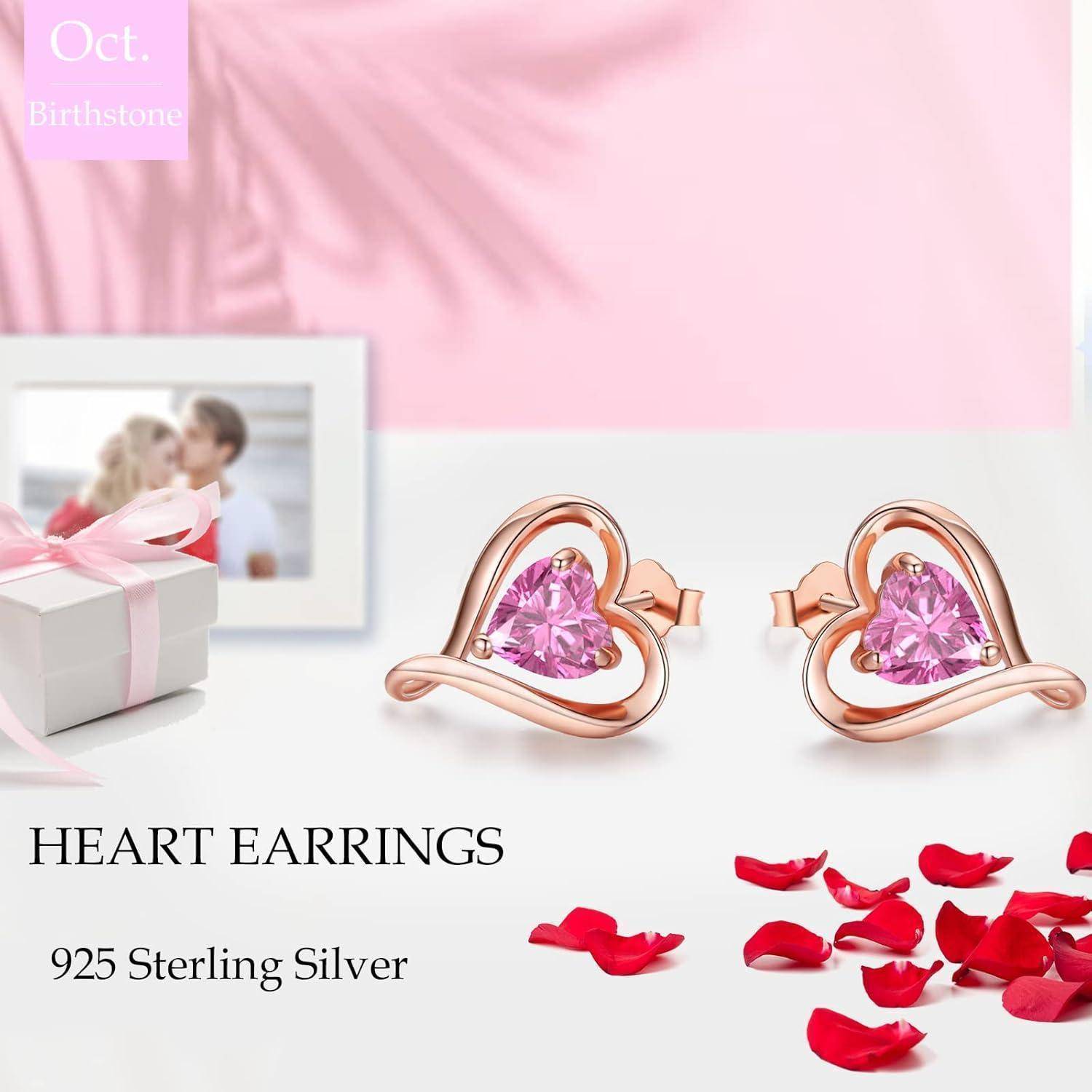 Herzförmige rosa Edelsteinohrringe in 925er Sterlingsilber mit Roségold-Akzenten. Hintergrund zeigt Rosenblütenblätter und eine Geschenkbox.