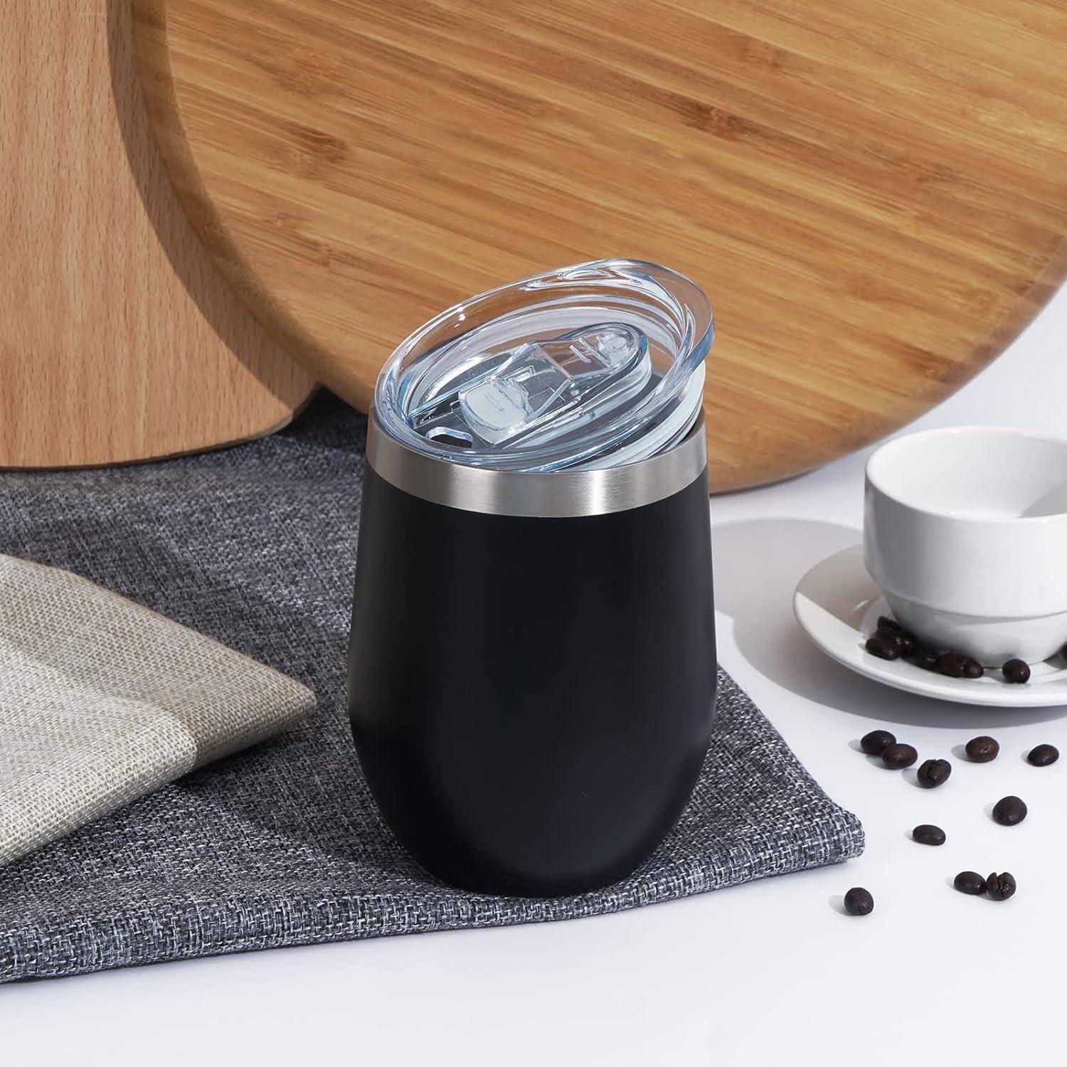 Ein schwarzer isolierter Becher mit einem transparenten Deckel steht auf einer grauen Matte neben einer weißen Tasse und Untertasse, umgeben von Kaffeebohnen.