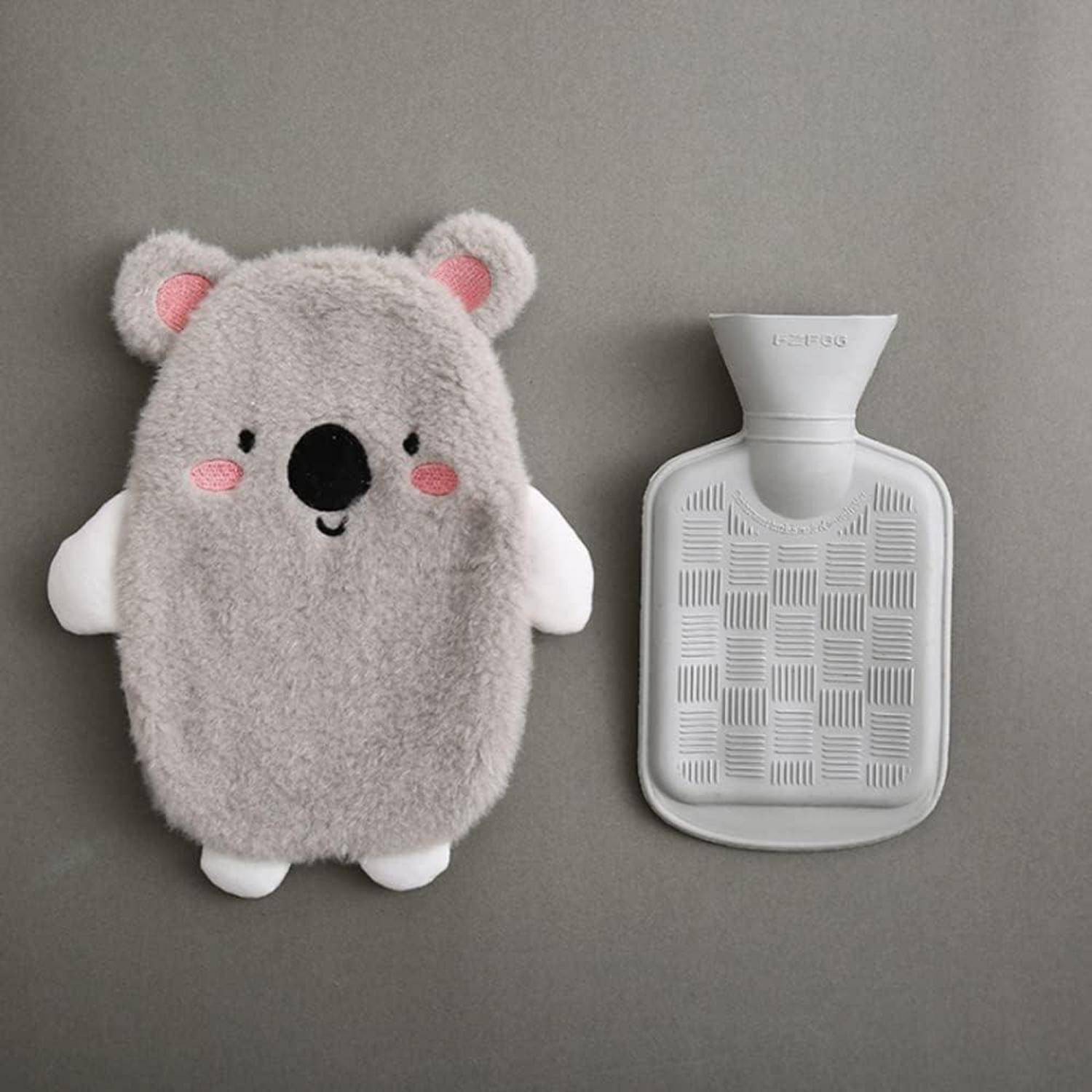 Eine graue, koalageformte Plüschhülle neben einer strukturierten Wärmflasche auf einer ebenen Oberfläche.