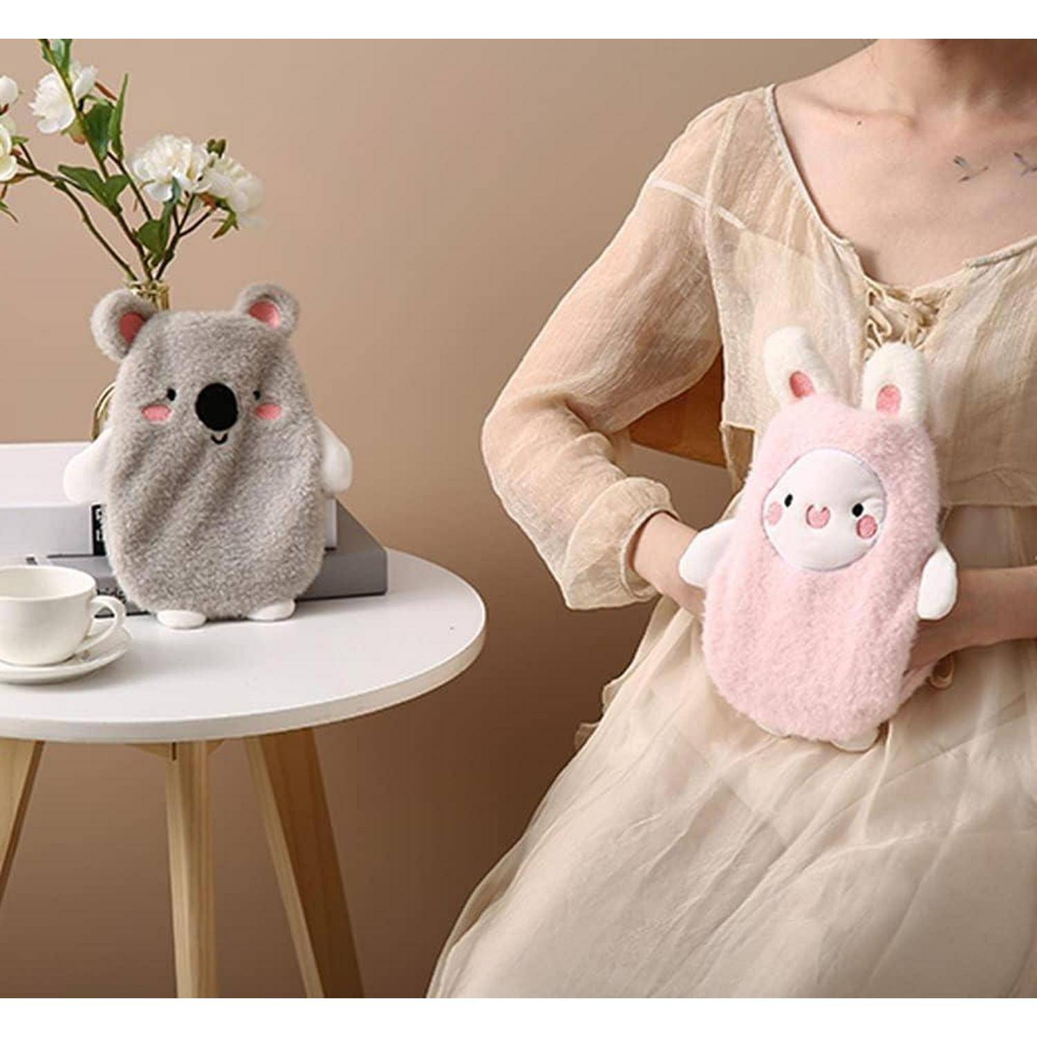 Eine Person sitzt an einem Tisch und hält einen rosa Plüschbezug mit Hasenmerkmalen, neben einem grauen Koala-Plüschbezug, einer Blumenvase und einer Teetasse.