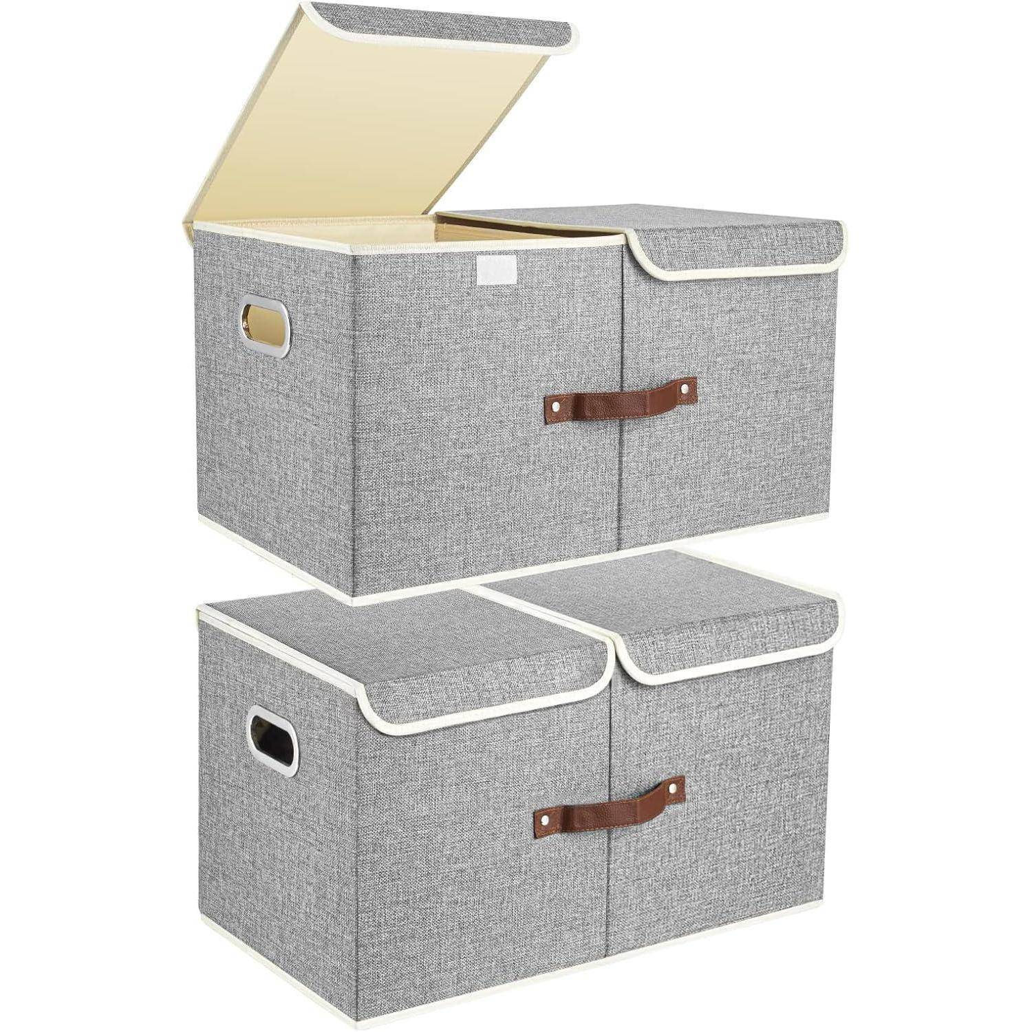 Gestapelte graue Aufbewahrungsboxen mit weißem Rand und seitlichen Griffen, ein Deckel geöffnet und einer geschlossen, mit braunen Lederriemen.