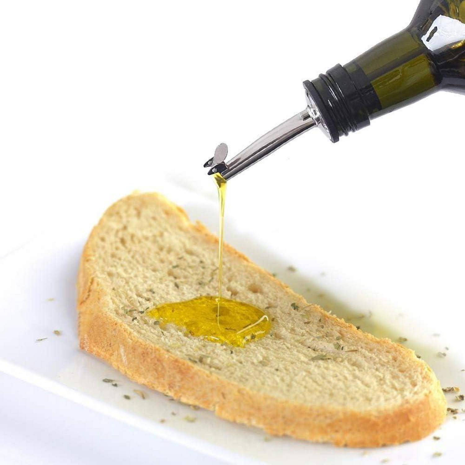 Ein Brotscheibe auf einem weißen Teller, die mit Olivenöl aus einer Flasche beträufelt wird.