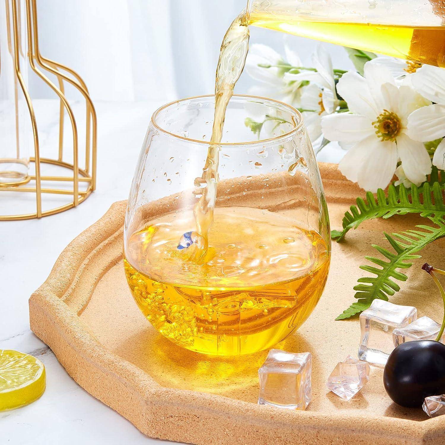 Ein Glas mit gelber Saft, der eingeschenkt wird, umgeben von weißen Blumen und Eiswürfeln auf einem Tablett, mit einer Zitronenscheibe in der Nähe.