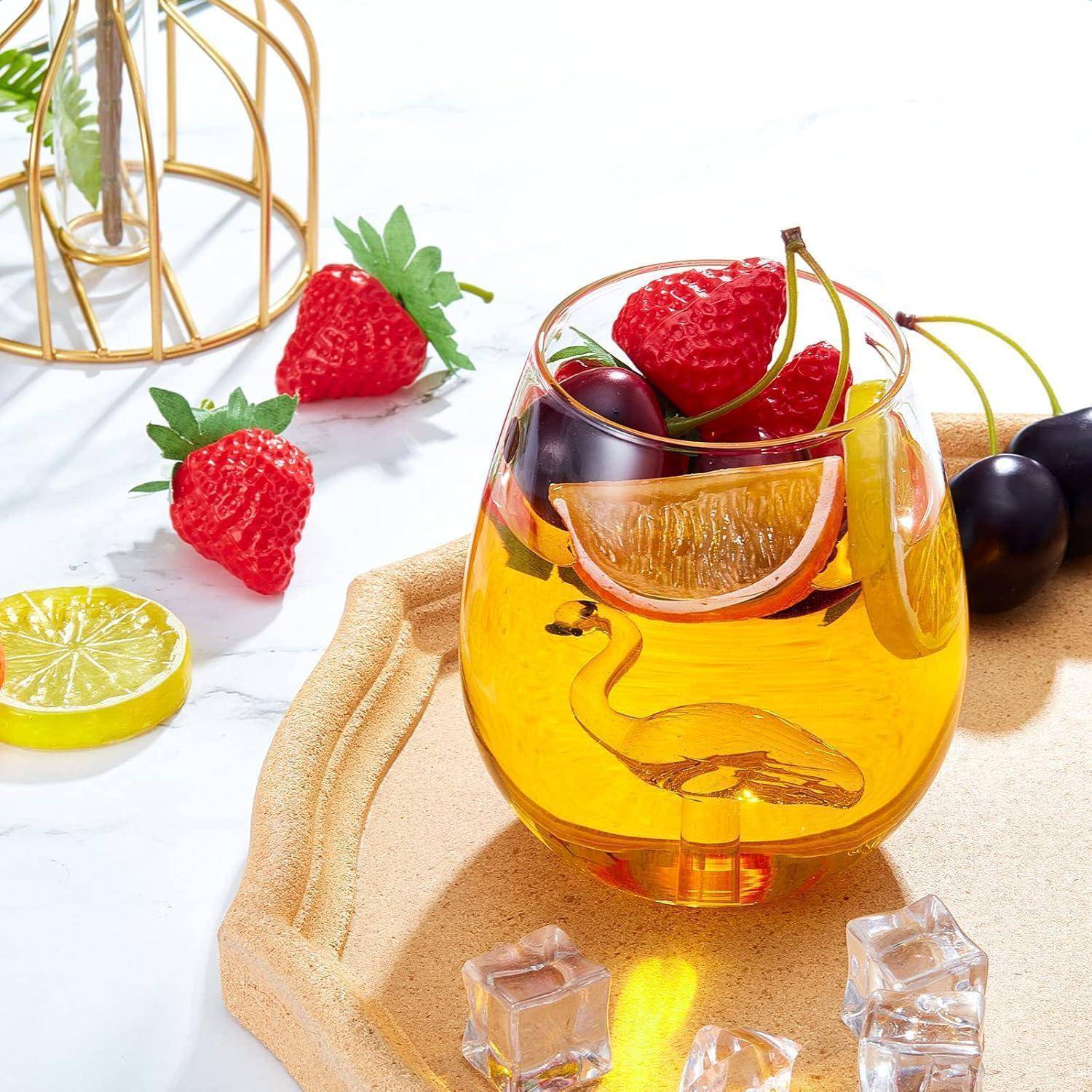 Ein Glas mit bernsteinfarbener Flüssigkeit und einem Schwanendesign, garniert mit Himbeeren und Kirschen, steht auf einem Holztablett. In der Nähe befinden sich Eiswürfel, Erdbeeren und eine Zitronenscheibe.