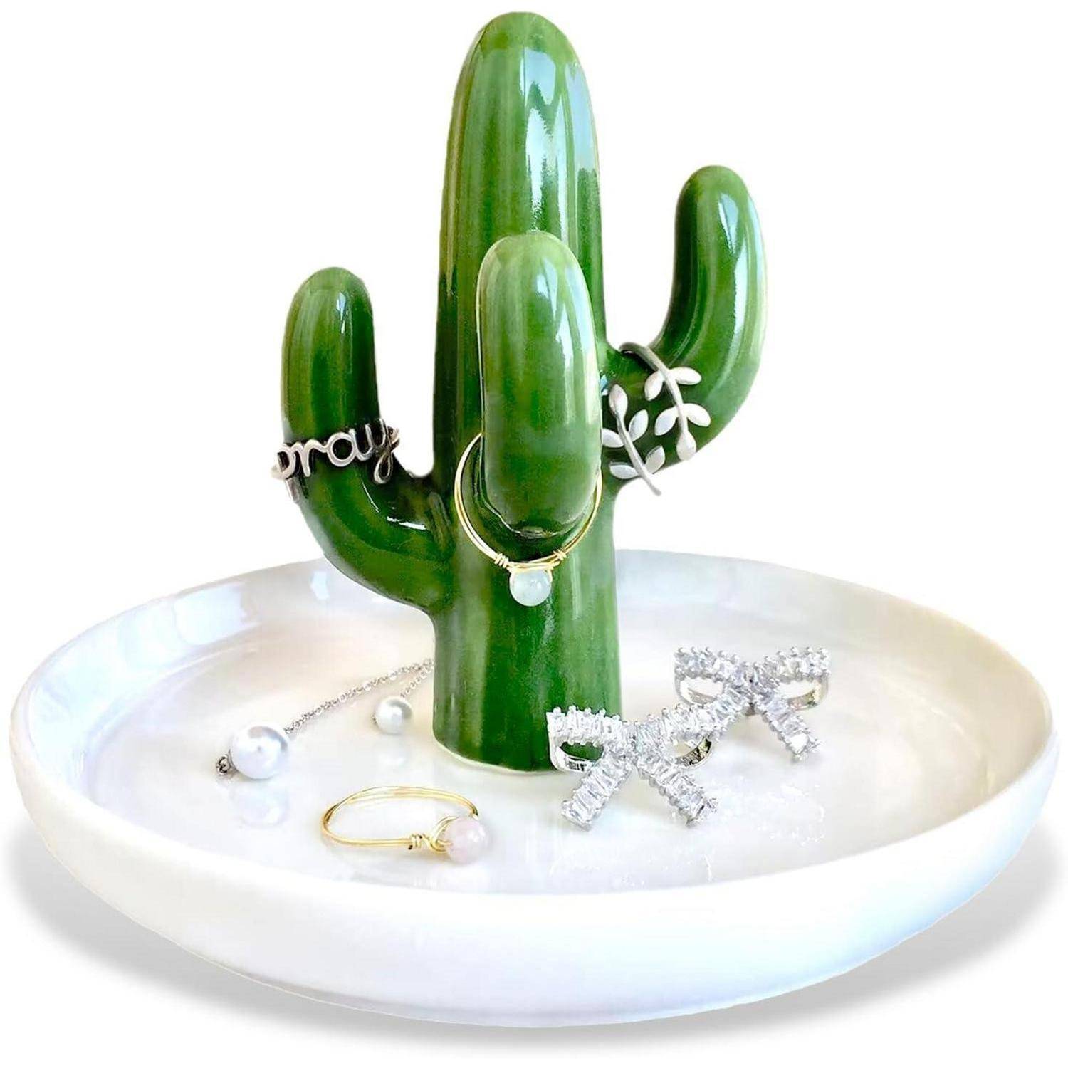Ein Schmuckhalter in Form eines Kakteens aus Keramik auf einem weißen Teller, geschmückt mit Ringen und Ohrringen, der eine moderne und dekorative Art der Accessoire-Organisation präsentiert.